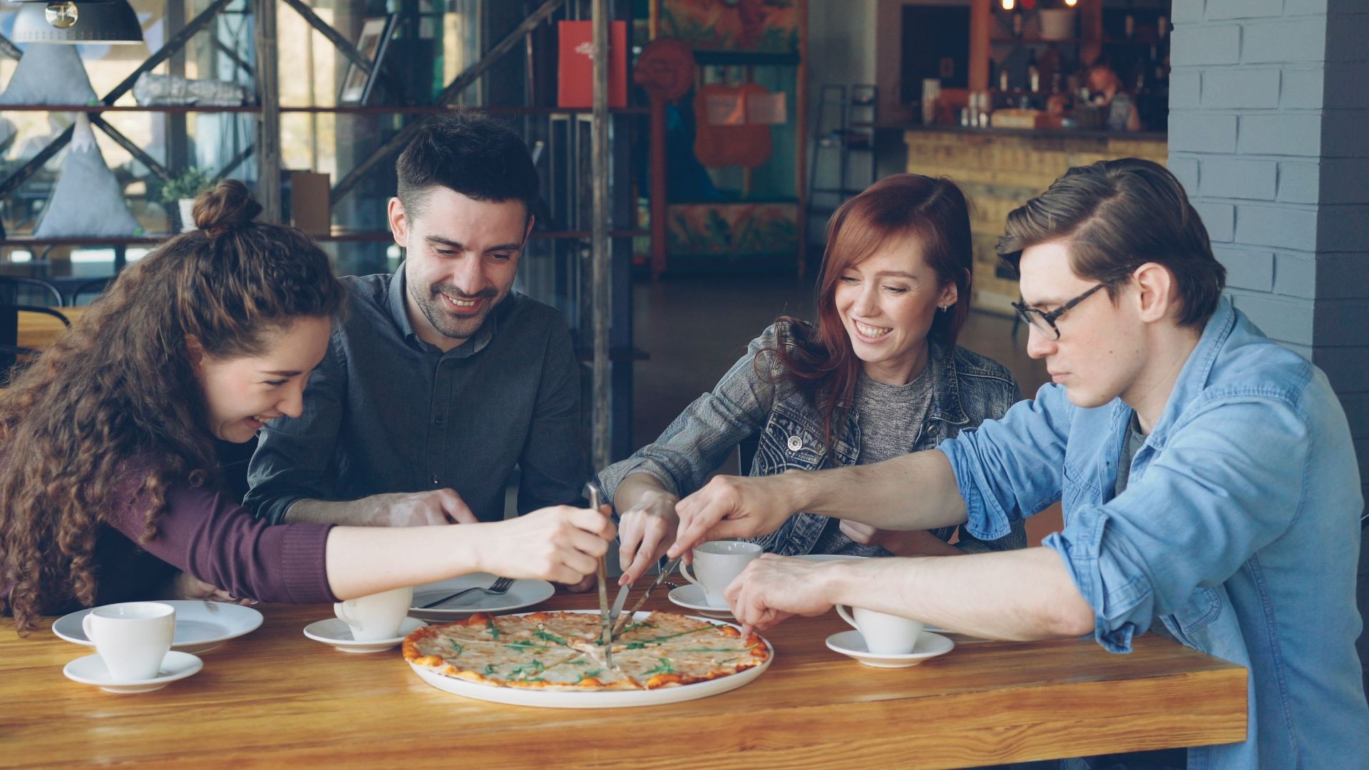 Group of young adults sharing a pizza at a cozy cafe. Perfect casual dining scene.