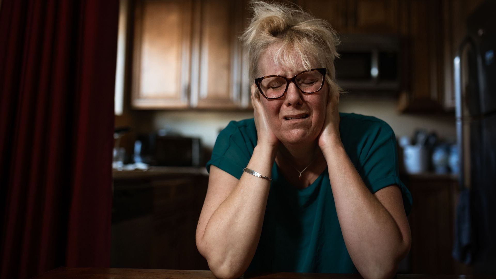 An adult woman in distress sitting at a table indoors, conveying emotional struggle.