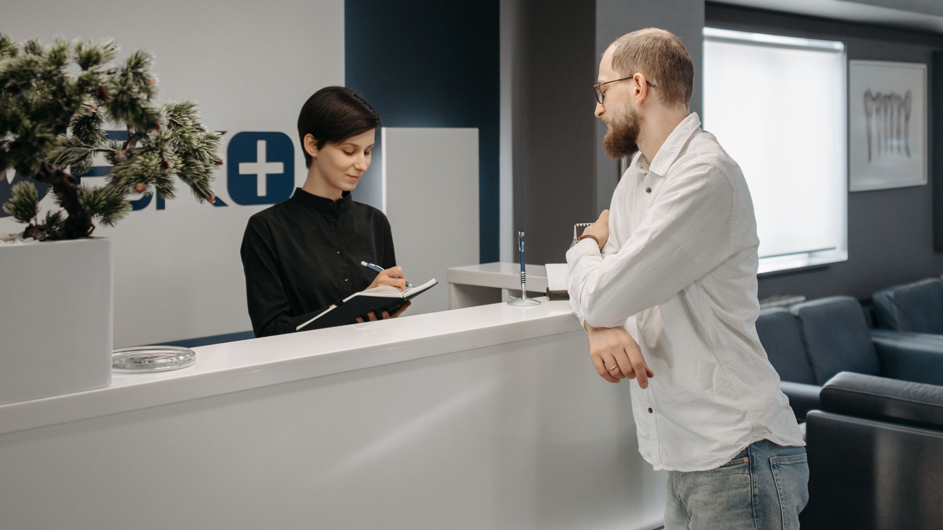 A man consults a receptionist in a modern clinic setting with contemporary design.