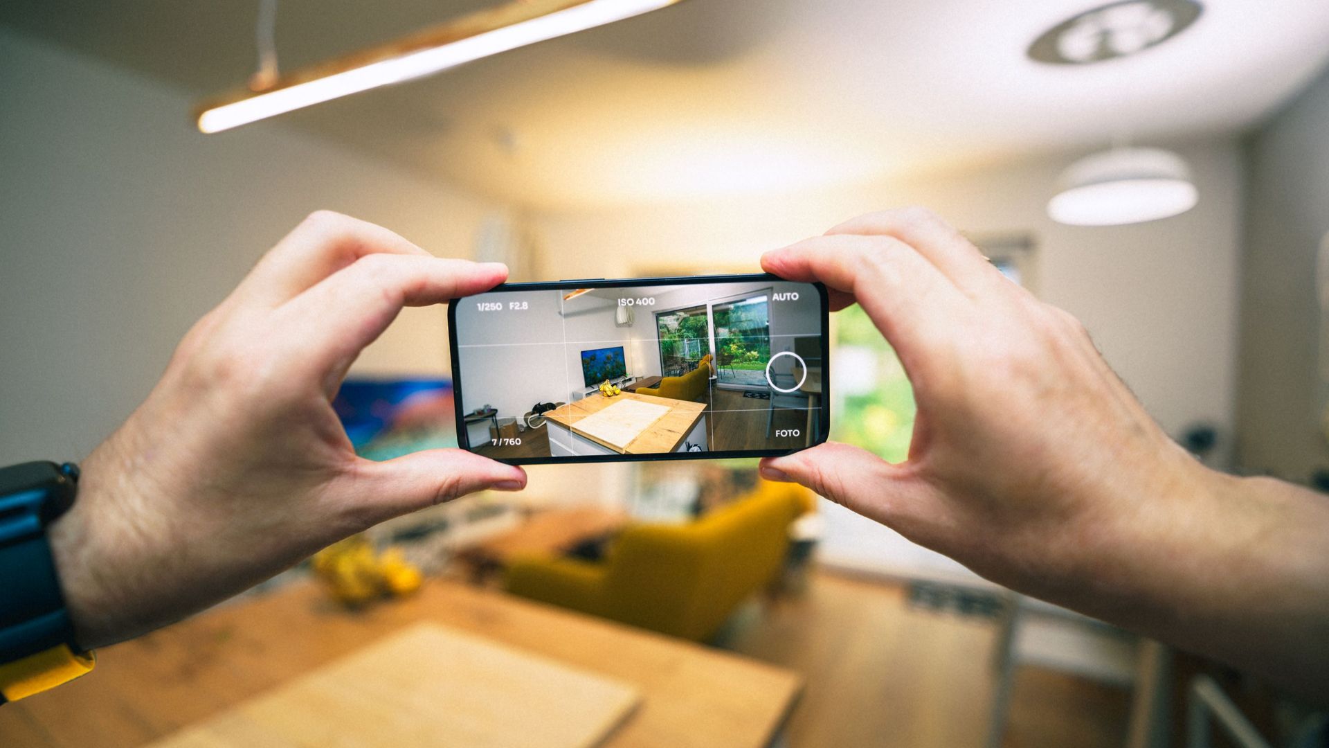 Hands capturing a modern living room interior with a smartphone.