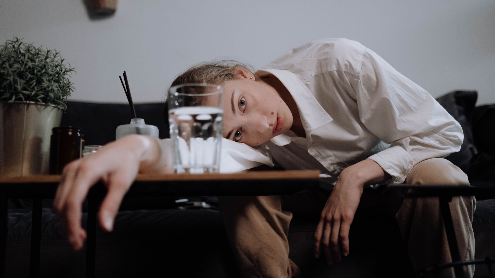 Young woman in white shirt, head resting on table, overwhelmed and fatigued at home.