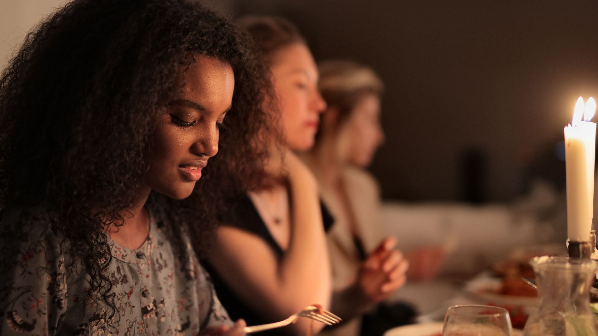 A diverse group enjoying a cozy, candlelit dinner together indoors.