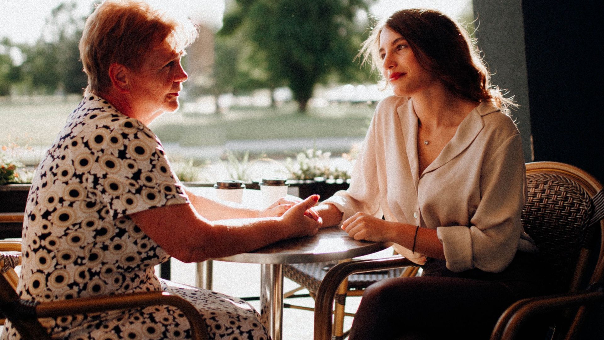A mother and daughter share a heartfelt moment while sitting at a café table outdoors.