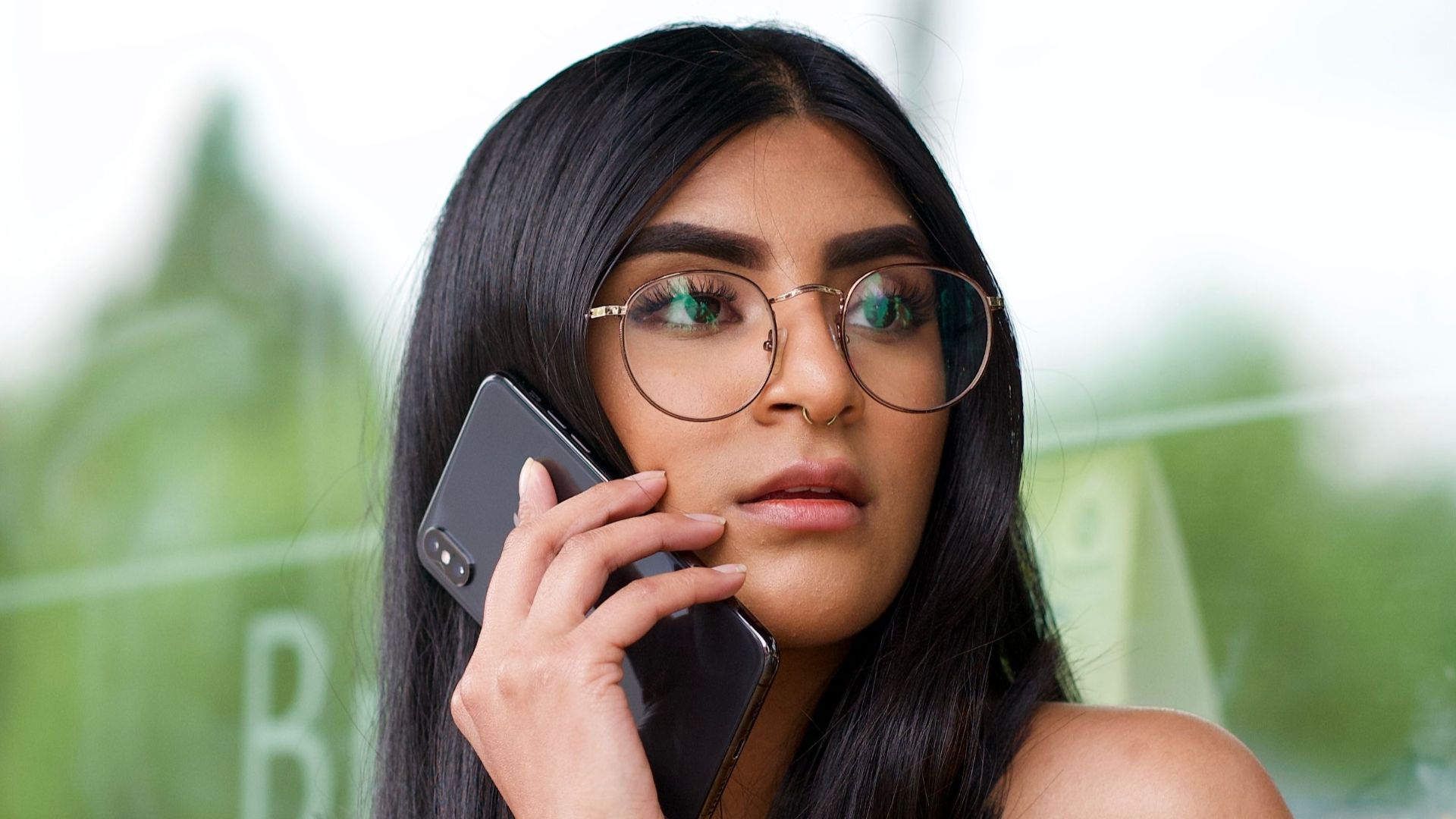 Stylish young woman with glasses sitting outside, making a phone call.