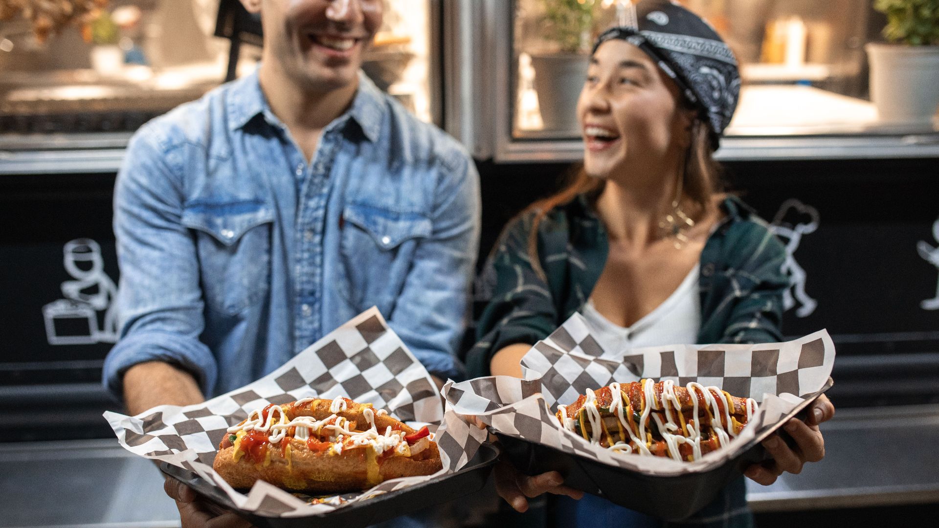 Laughing couple holding gourmet street food outside a food truck at night.