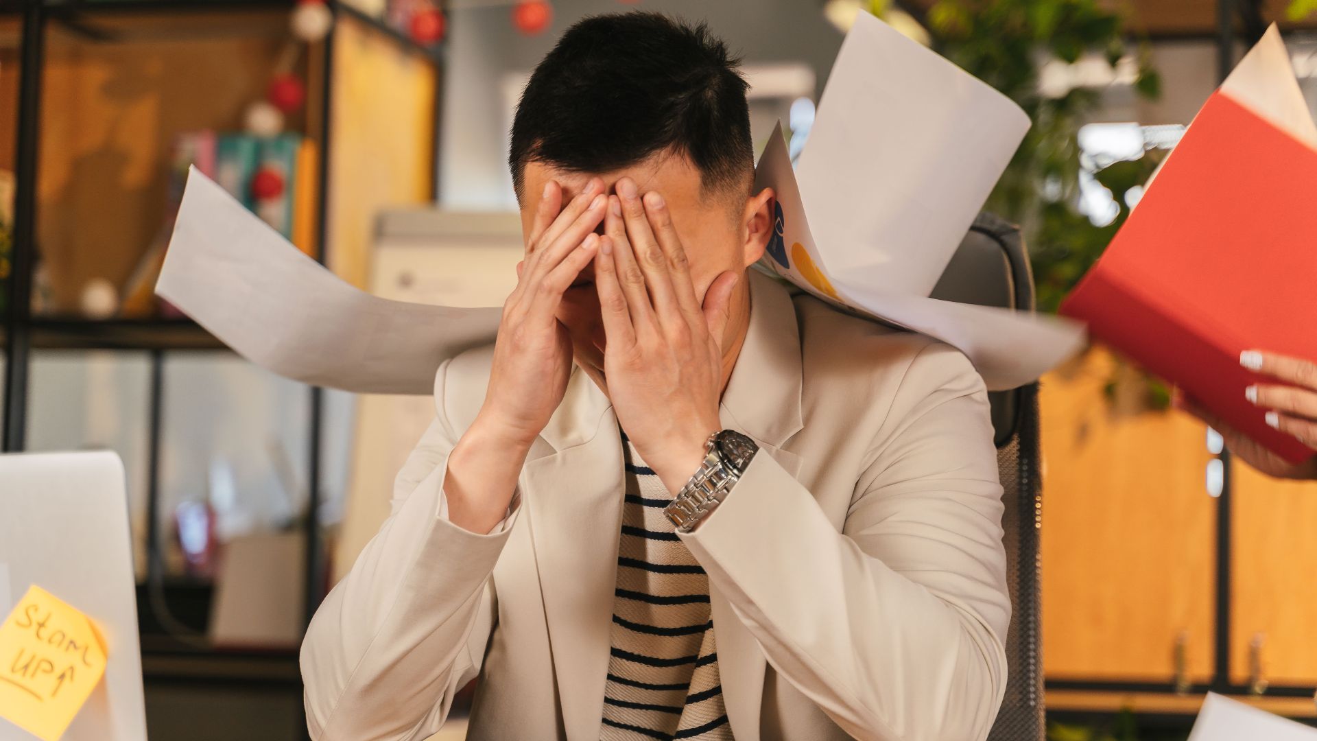 Stressed businessman overwhelmed by paperwork in office environment, demonstrating burnout.