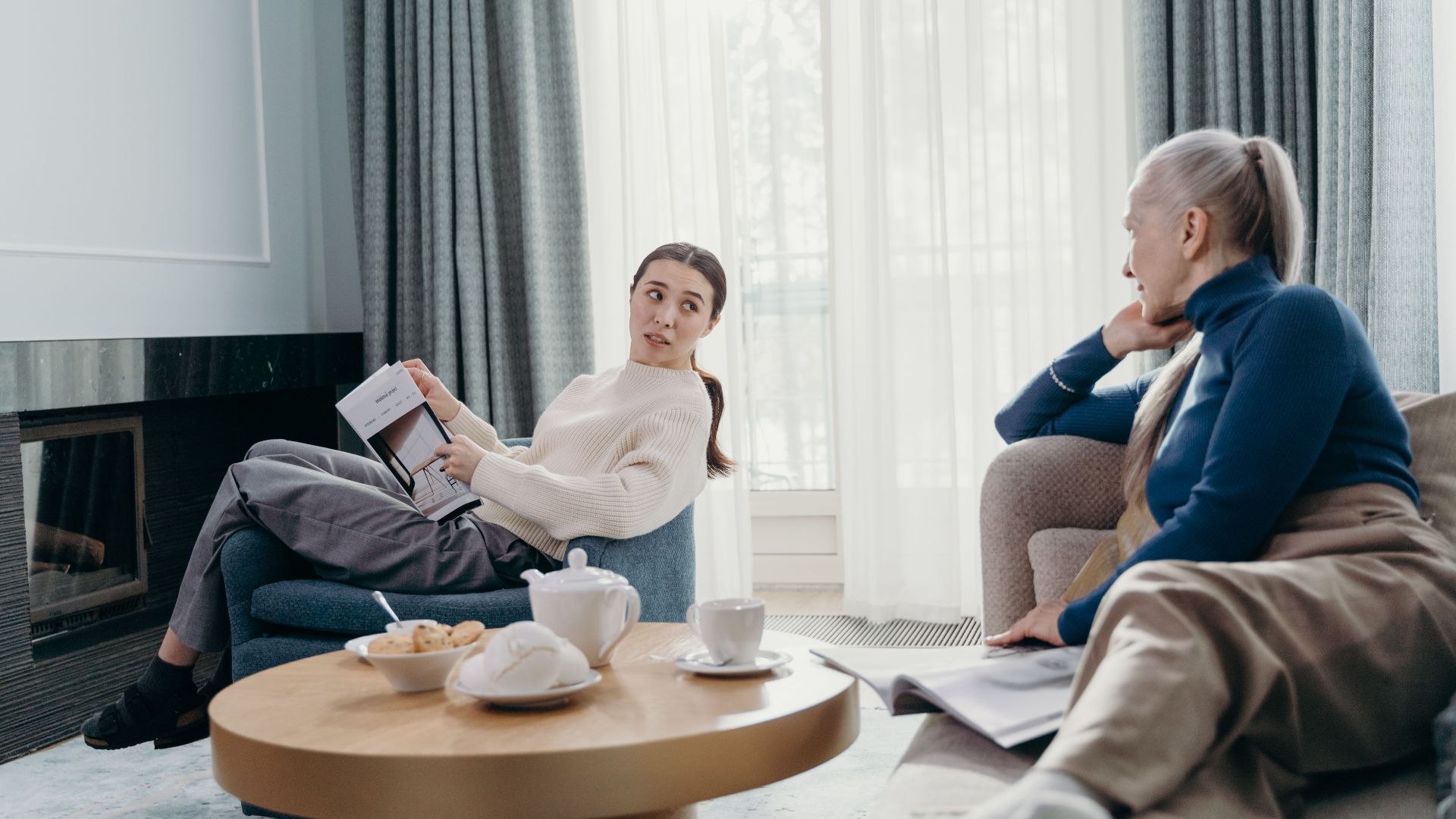 Two women engage in a relaxed conversation in a modern living room setting.