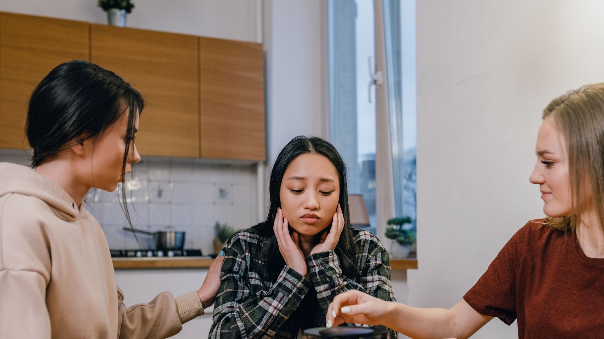 Three women gathered at a kitchen table, offering comfort and support to a sad friend.