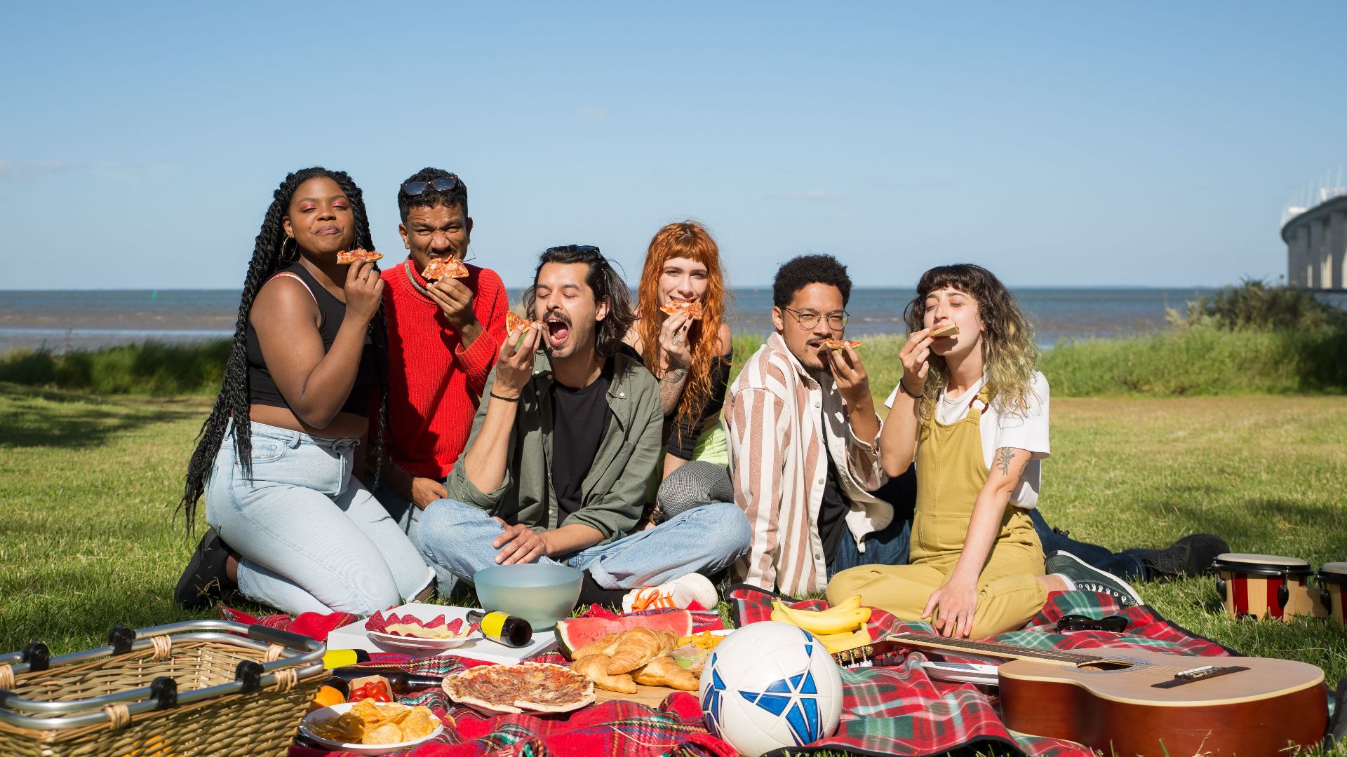 Friends enjoying a sunny picnic by the beach in Portugal, savoring food and fun.