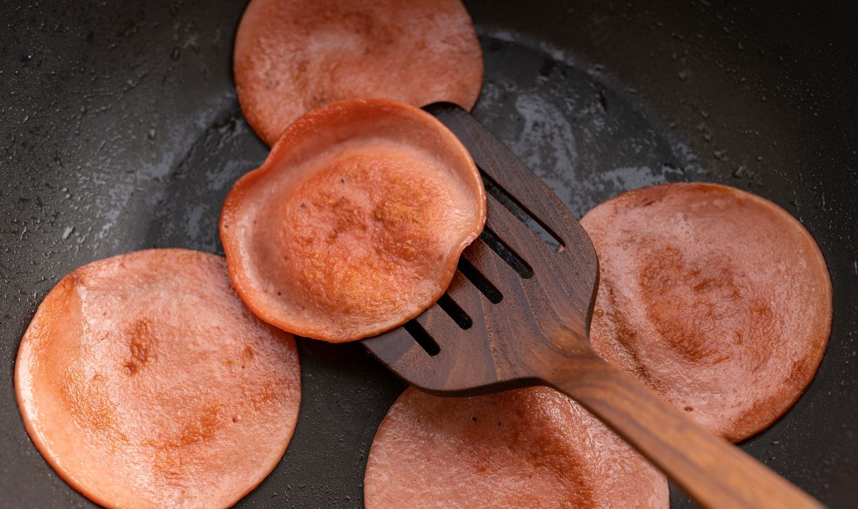 closeup frying pork bologna in black pan with small amount of cooking oil