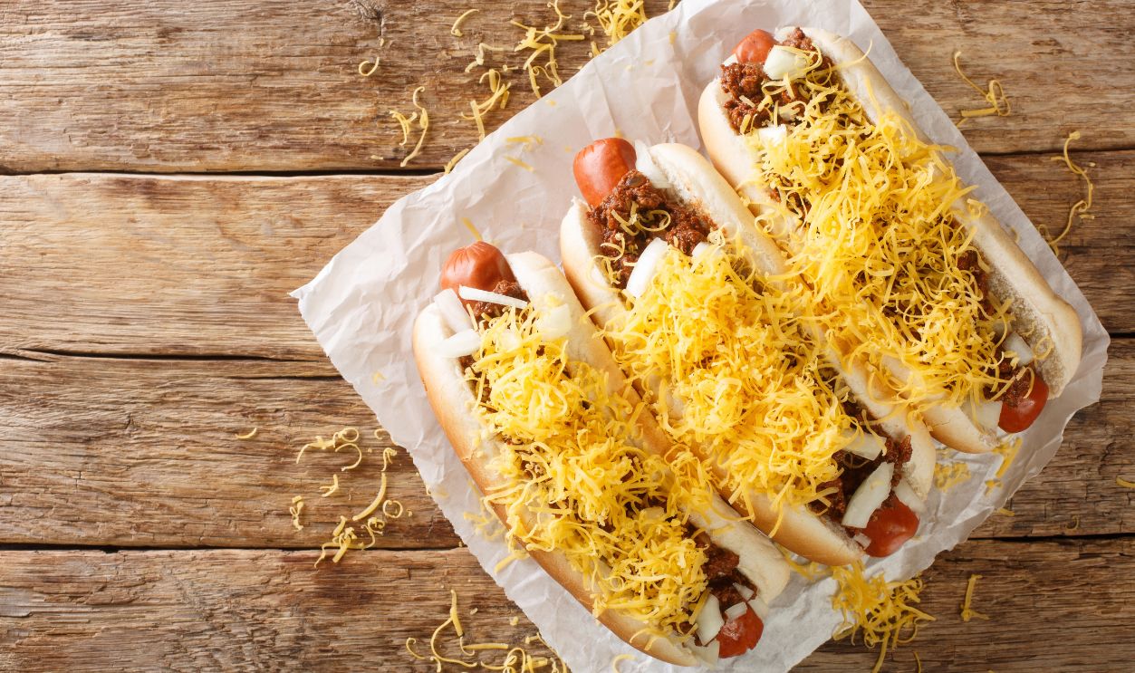 American Cincinnati Chili hot dog closeup in the paper on the table. Horizontal top view from above