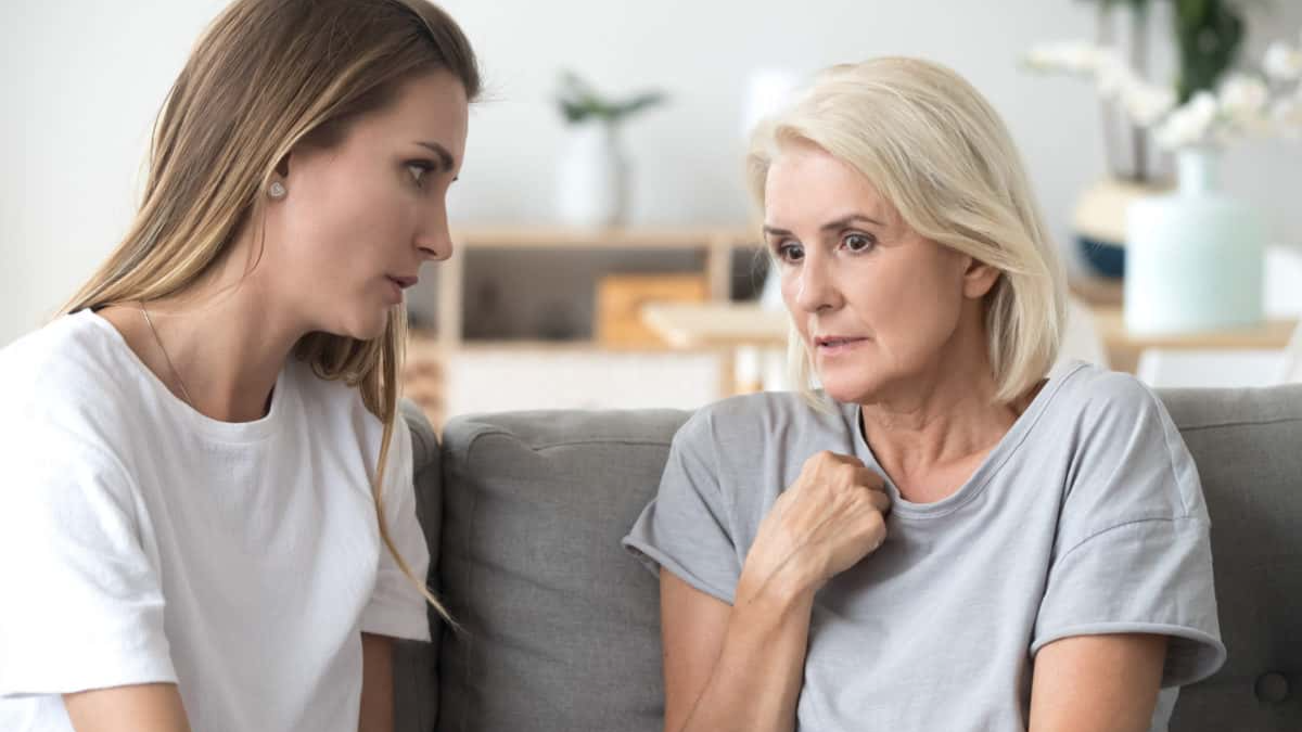 Concerned aged mother and adult daughter sit on couch having serious conversation, young woman talk with worried elderly mom, listen to her sharing problems or concerns, help dealing with depression