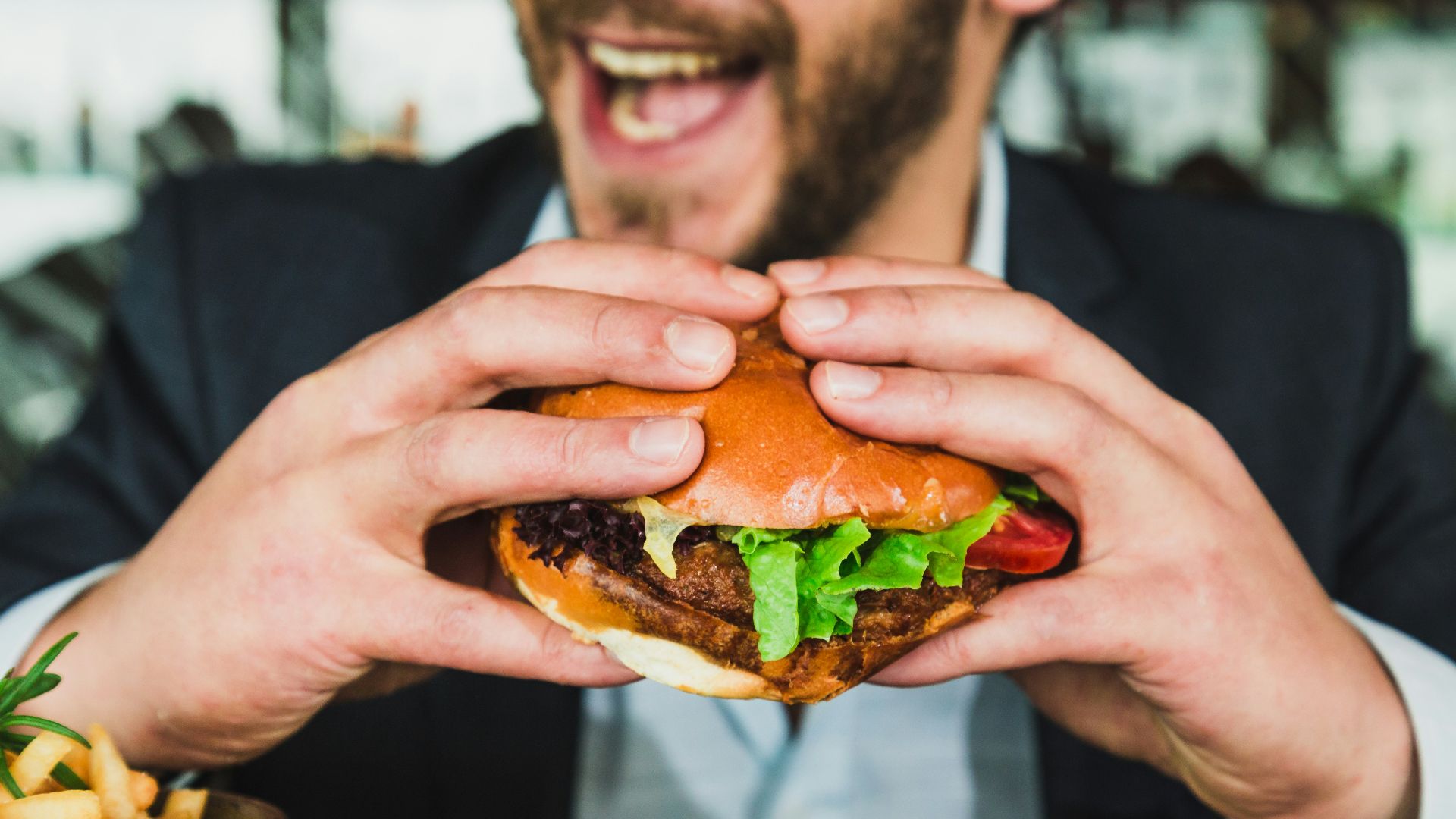 person holding burger bun with vegetables and meat