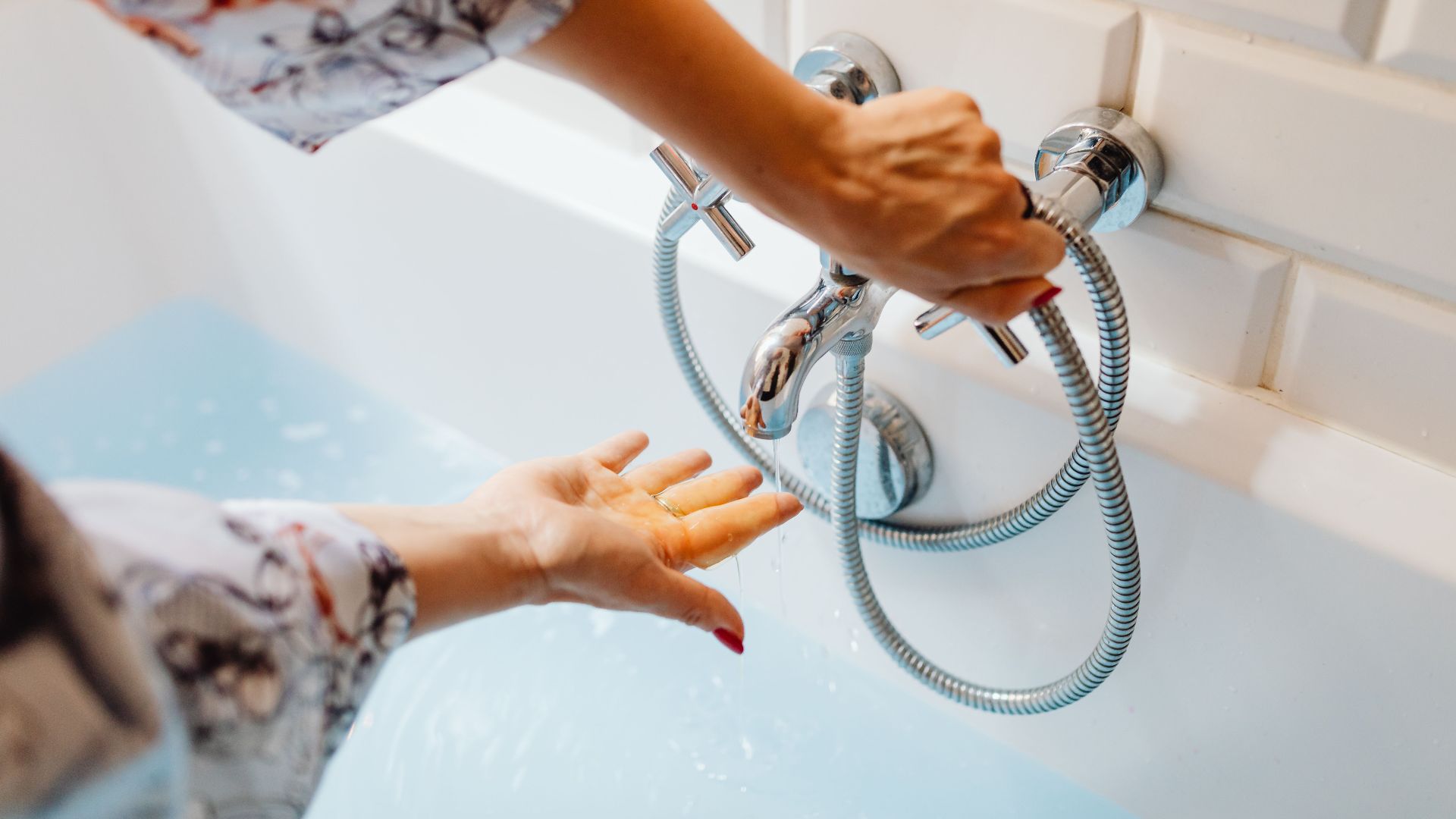 Close-up of hands adjusting water temperature of a bath faucet.
