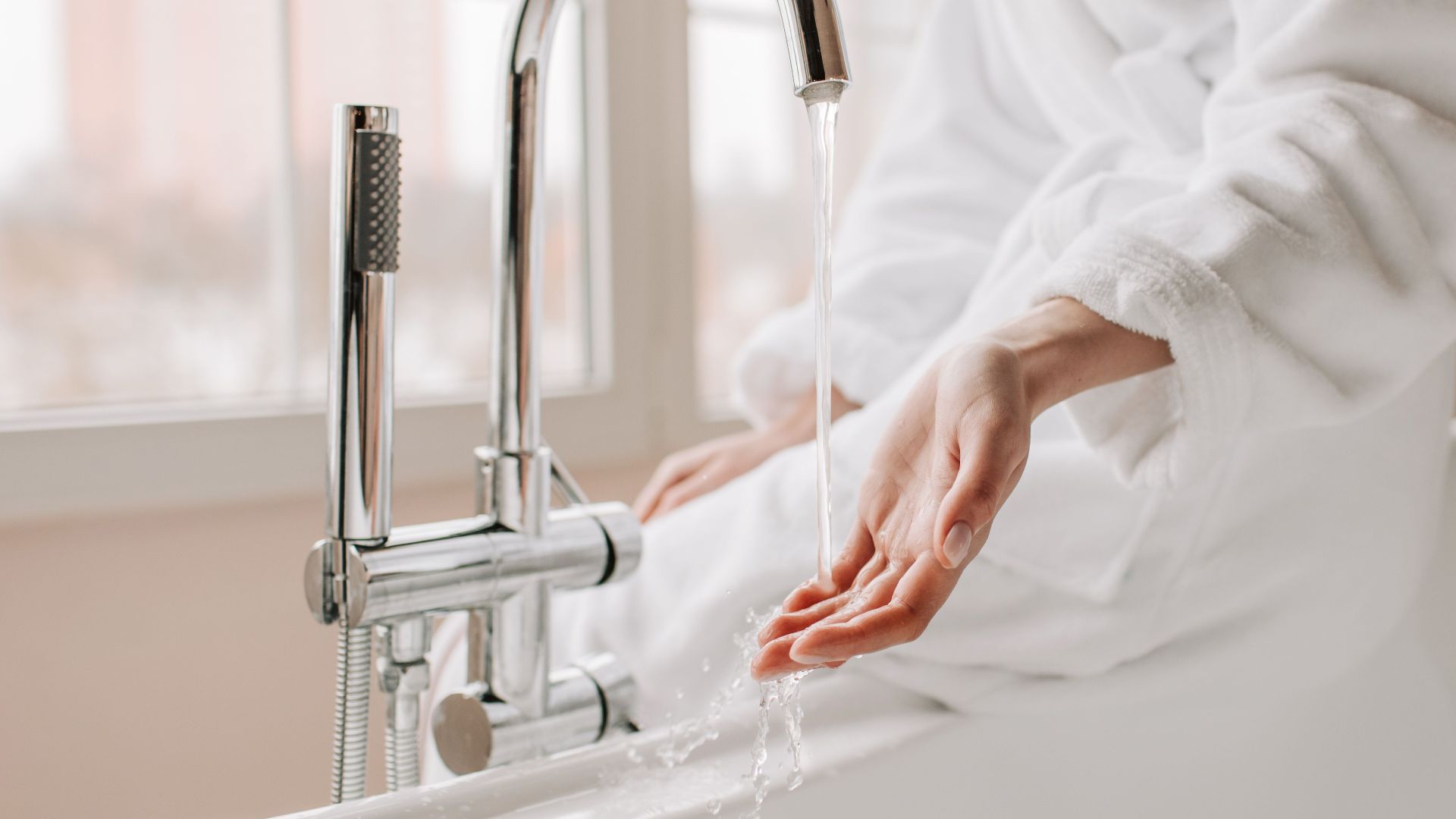 Close-up of a person in a bathrobe feeling the flowing water in a bathtub.