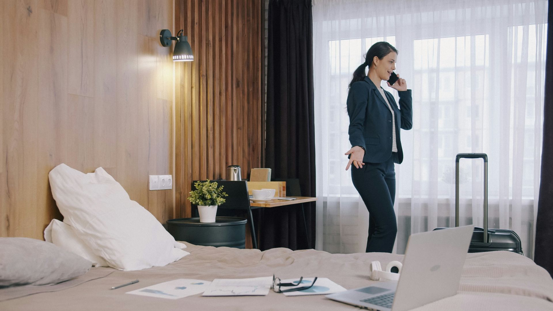 A woman in a dark suit talking on a phone in a hotel room