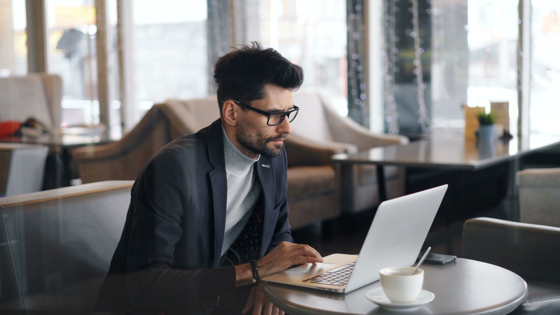 Focused businessman working on a laptop in a stylish café, drinking coffee.