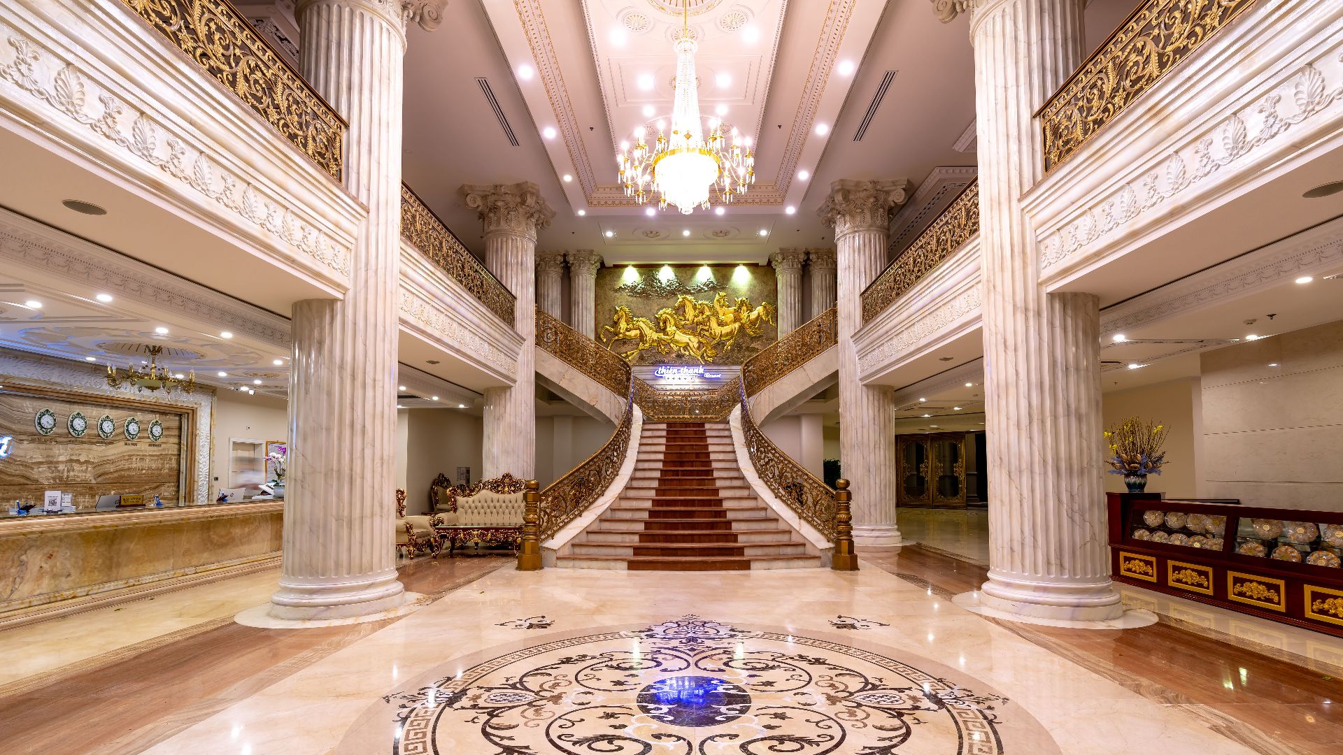 Elegant hotel foyer featuring a grand staircase, marble floors, and a dazzling chandelier.