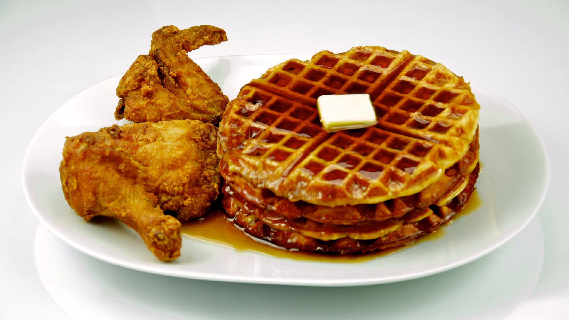 Fried chicken and waffles with maple syrup and butter on a white plate and shot on a white background.