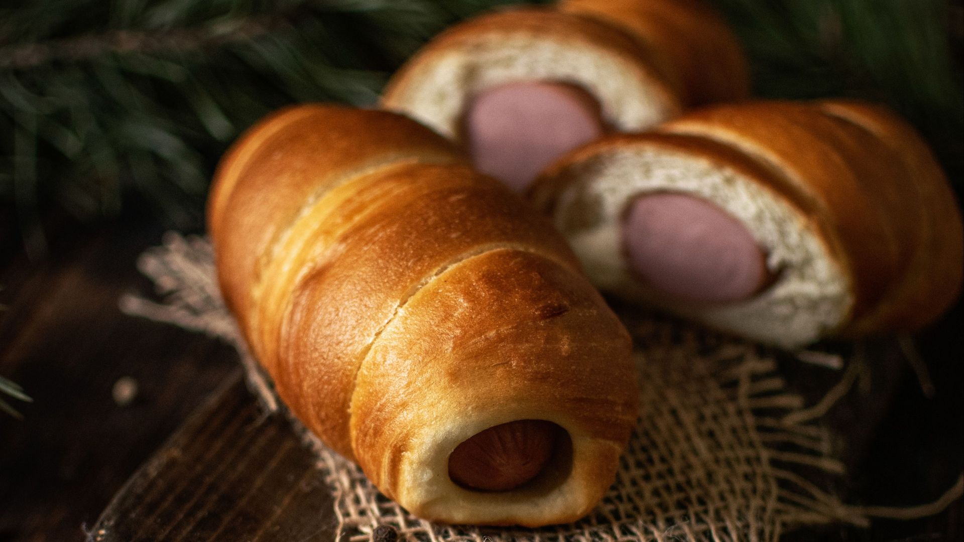 Gourmet hot dog rolls beautifully presented on a rustic wooden board, perfect for a savory meal.