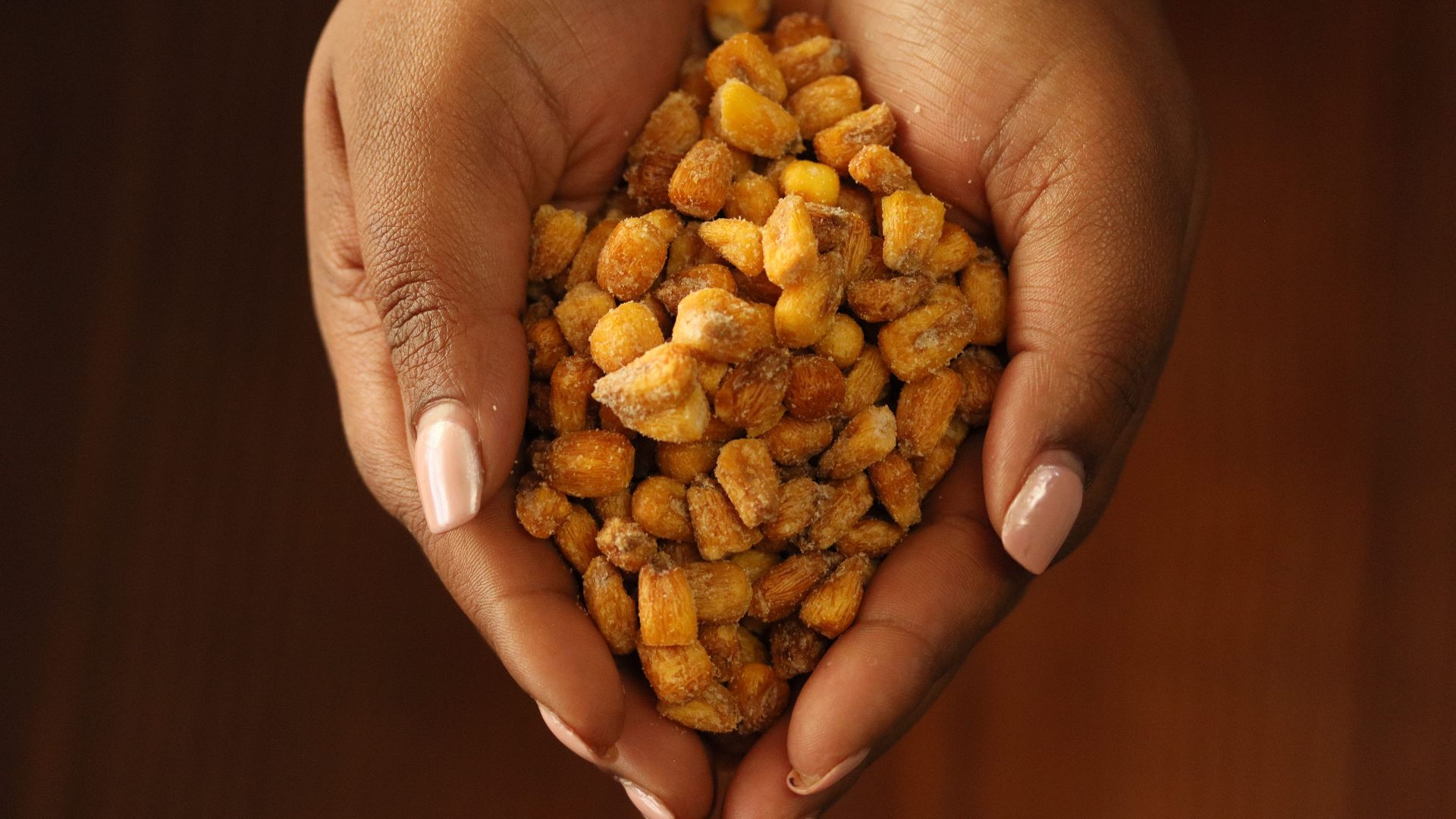 Close-up of hands holding crunchy roasted corn snacks on a wooden background.