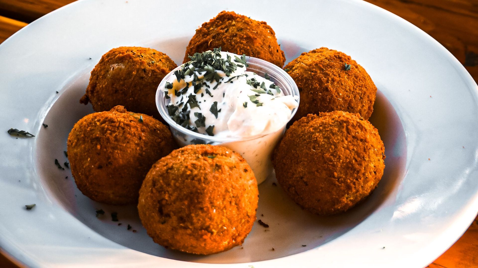 Close-up of crispy fried arancini balls with herb garnish served with creamy dip.