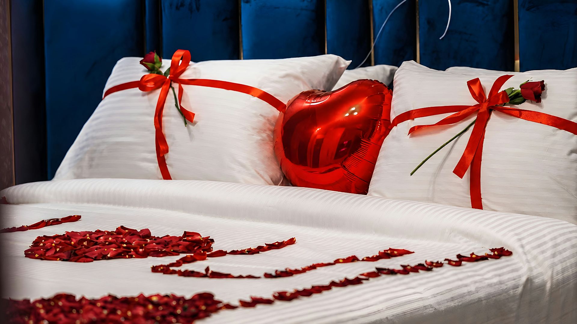 A bed decorated with red rose petals and heart-shaped items