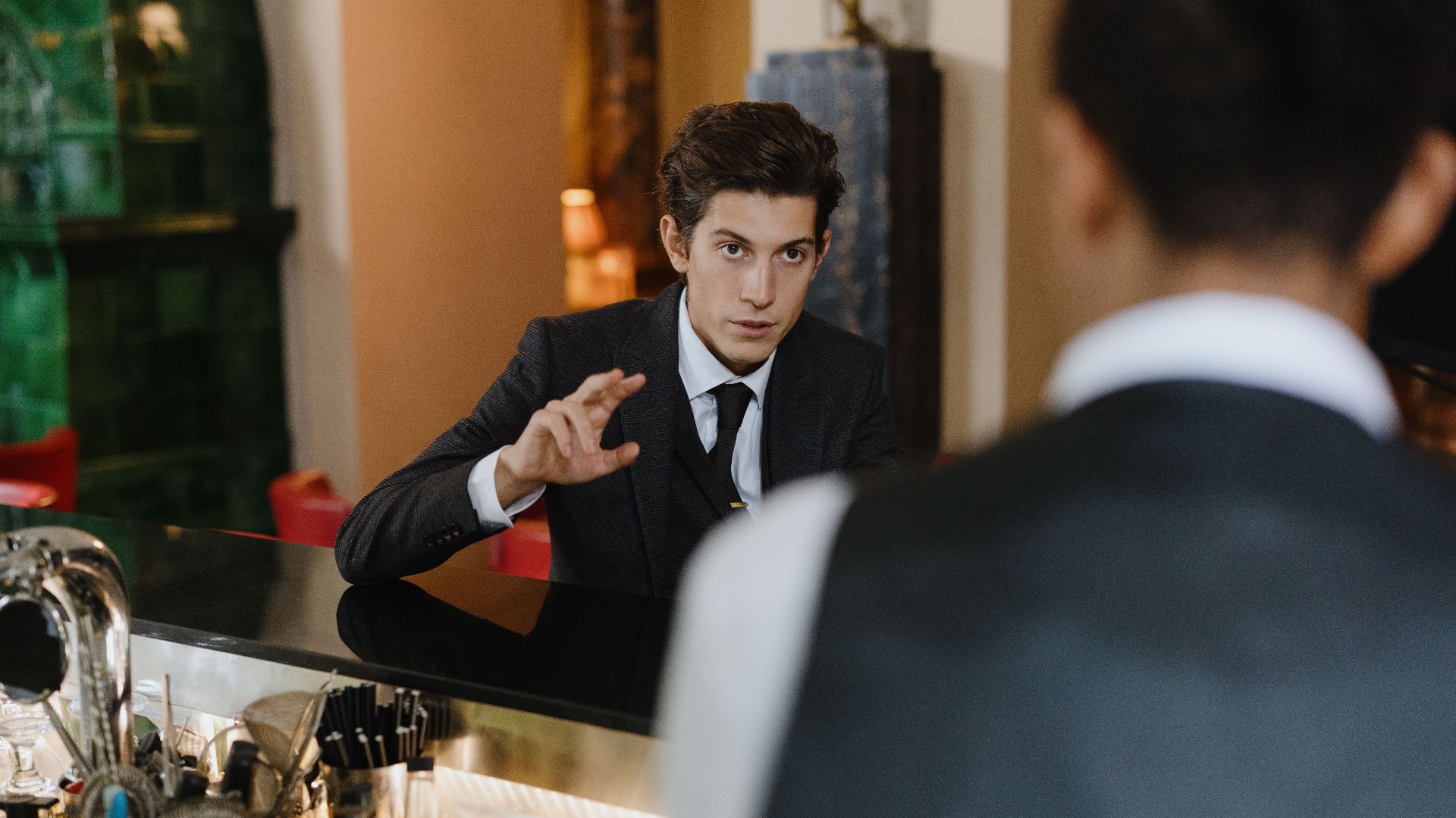 A classy interaction between a gentleman and a waiter at a stylish vintage bar setting.