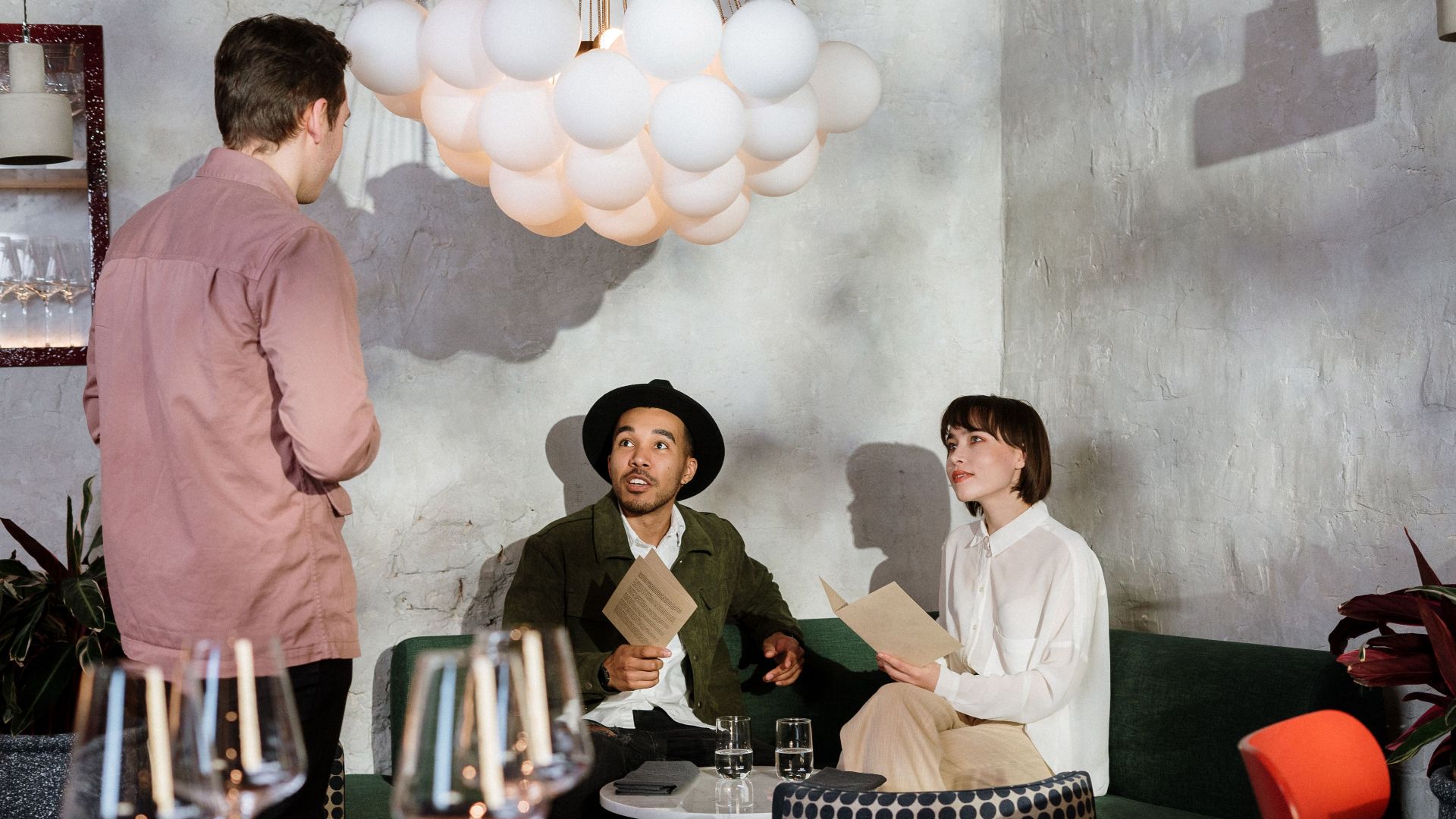 A couple reviews a menu at a chic restaurant, engaging with a waiter.