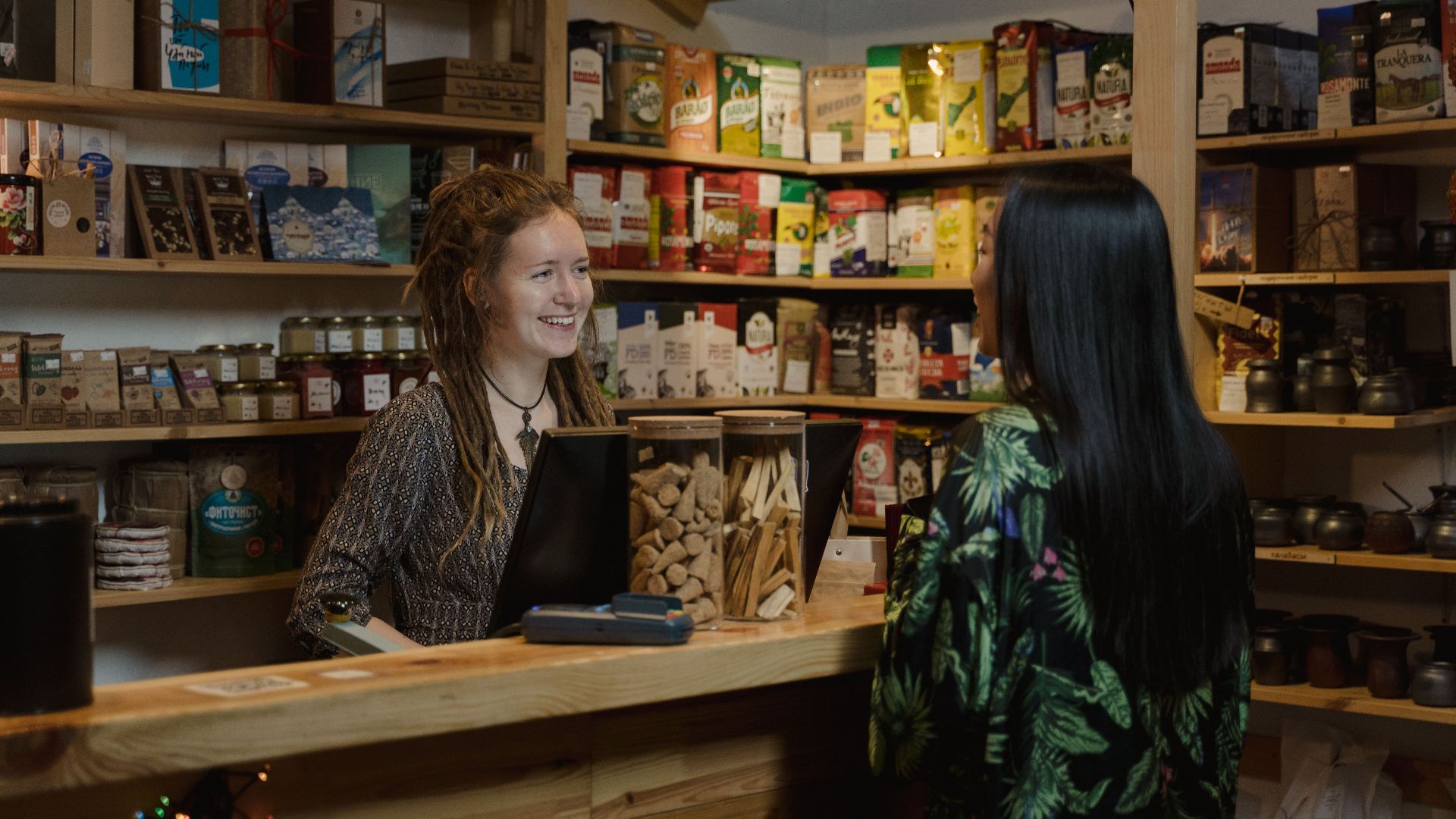 Friendly shopkeeper assisting a customer in a cozy, well-stocked store environment.