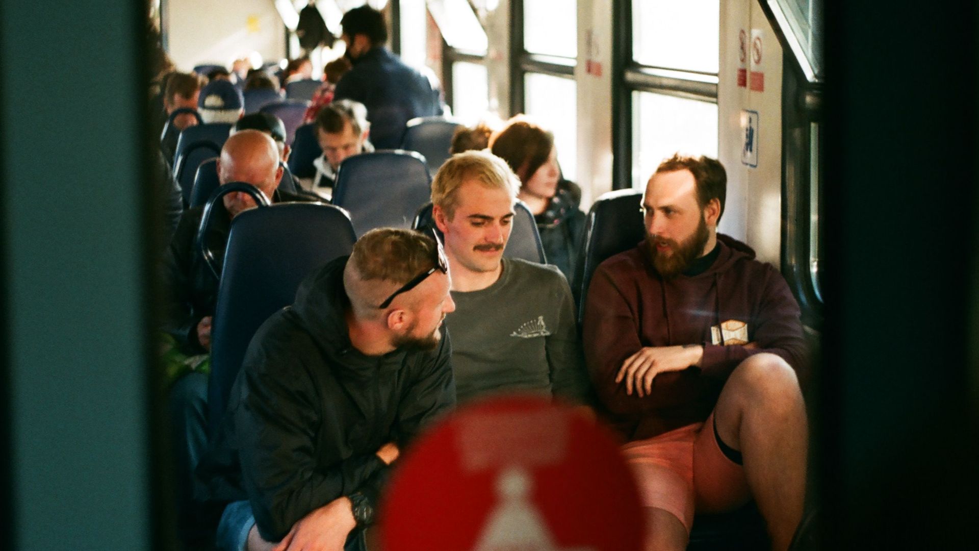 Three men engaged in conversation on a crowded train during daytime travel.