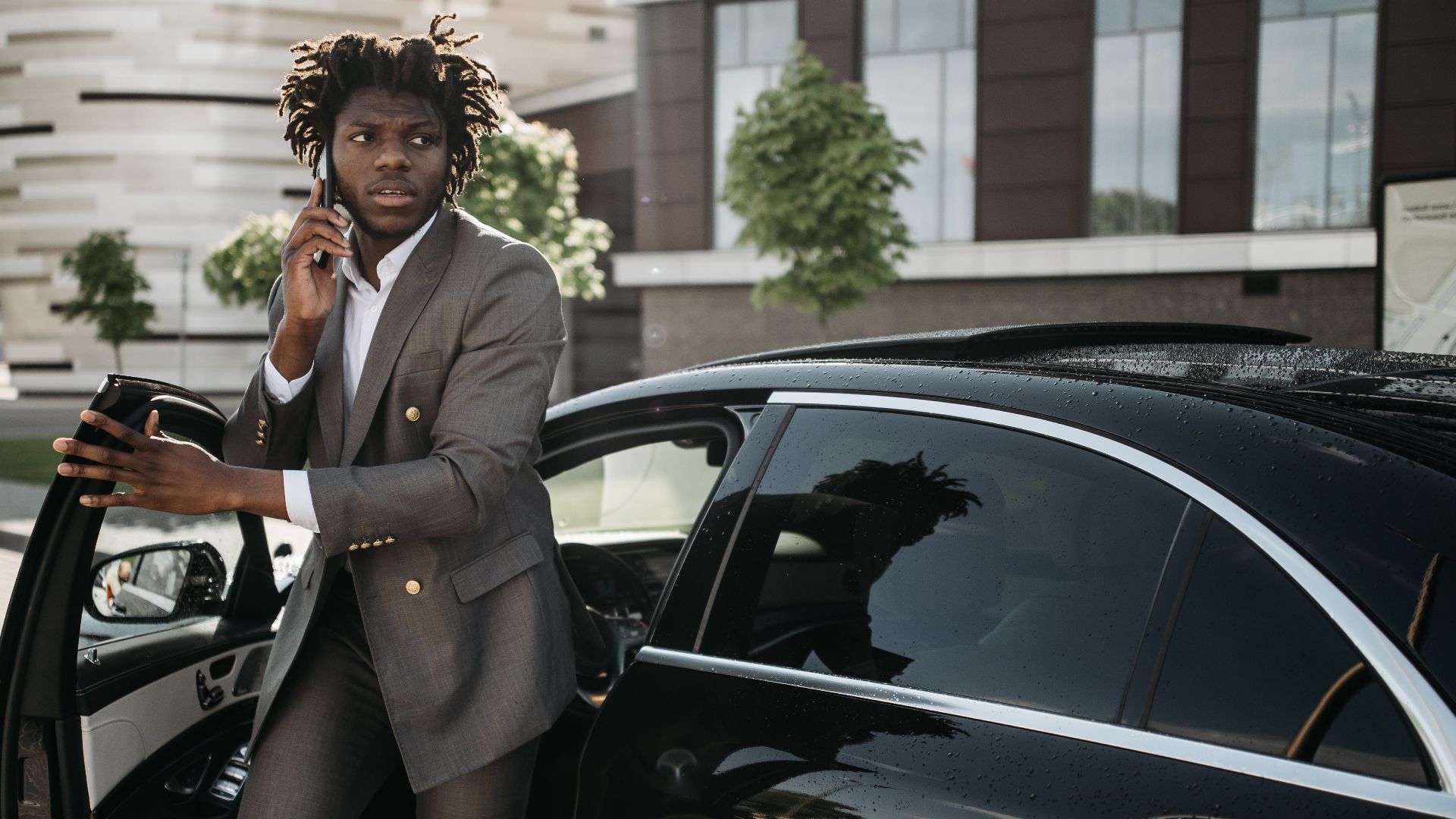 Confident businessman in a suit talking on a smartphone while getting out of a luxury black vehicle.