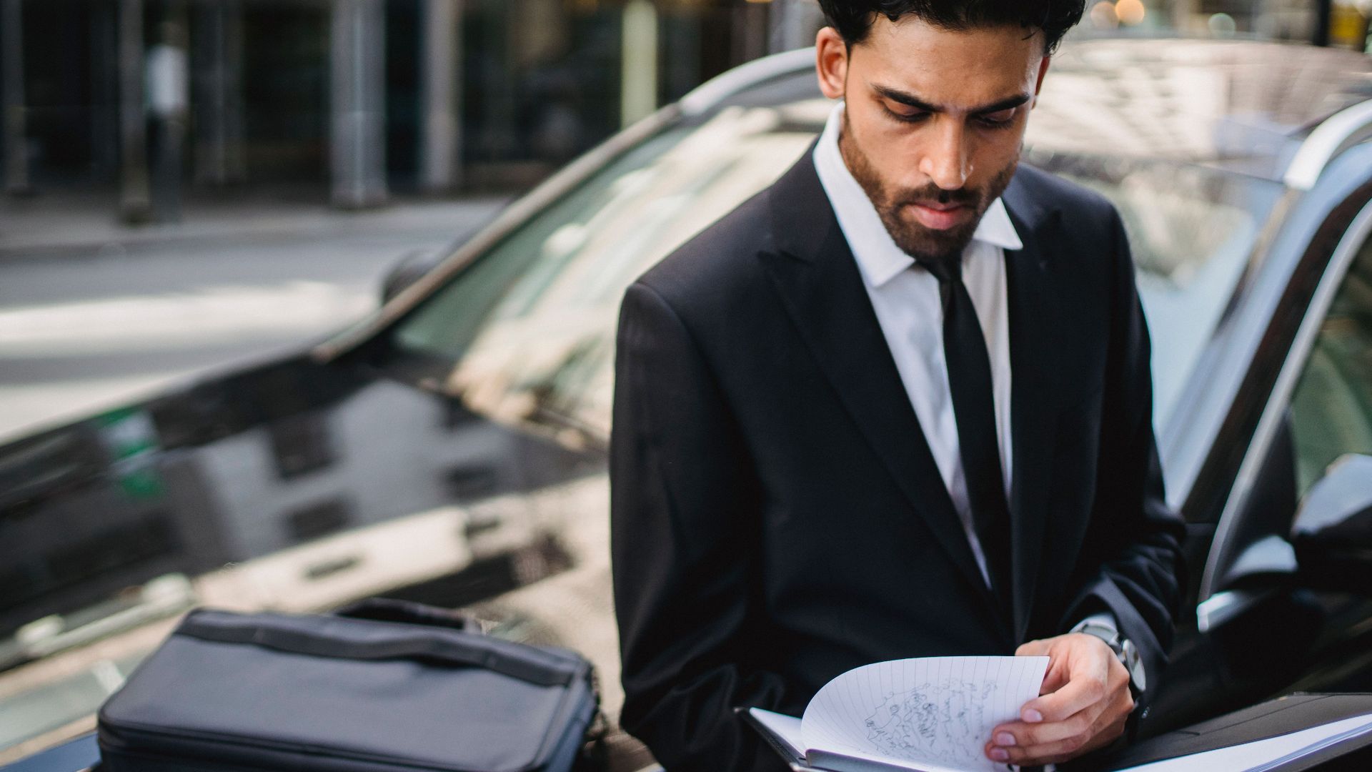 Confident businessman reviewing documents on the street beside a car.