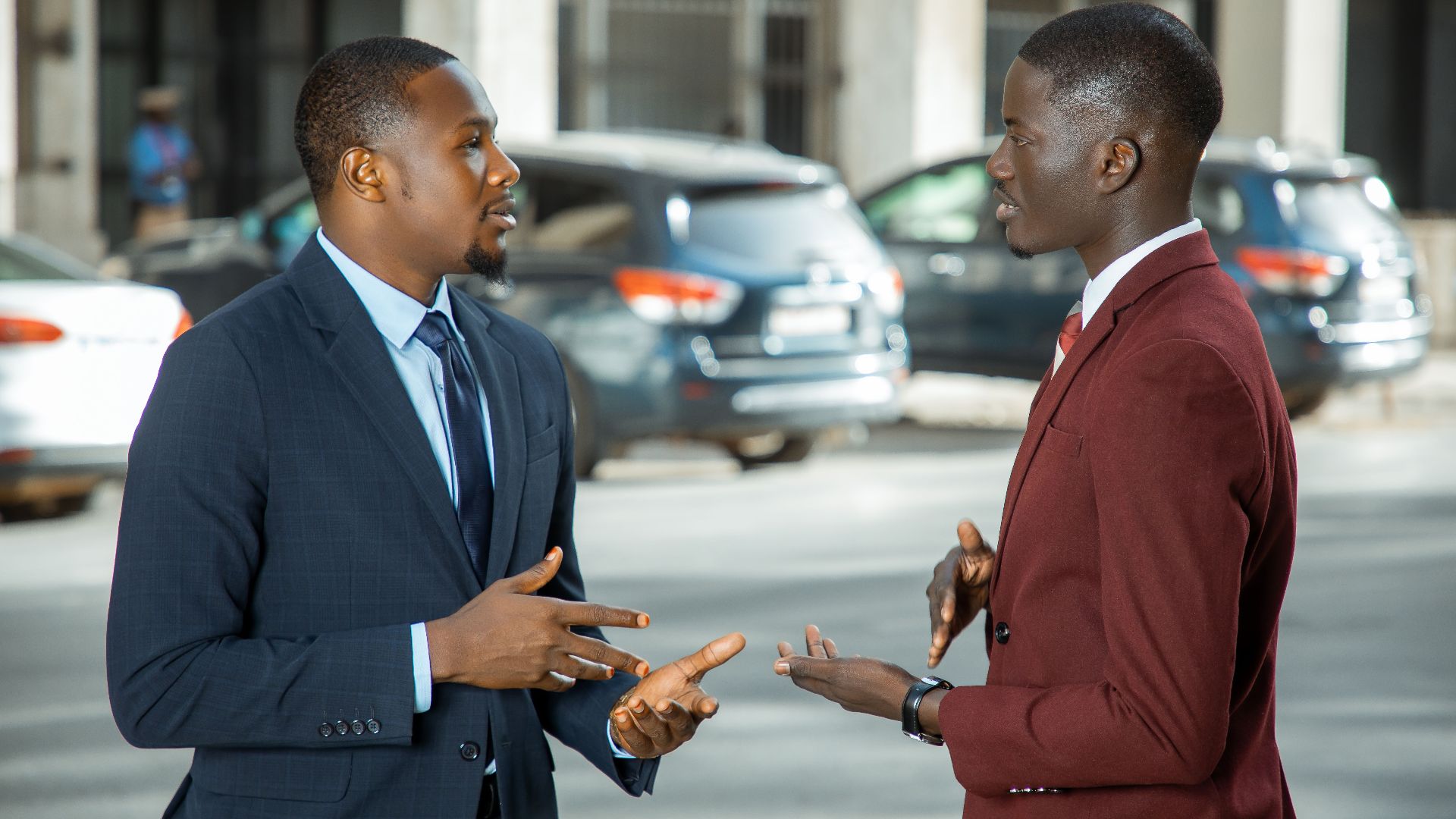 Two African businessmen in formal suits have a discussion on a city street in Dakar, Senegal.