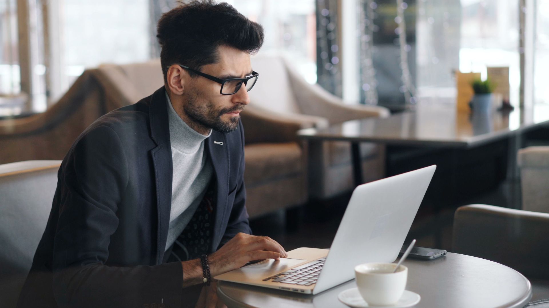 Focused businessman working on a laptop in a stylish café, drinking coffee.