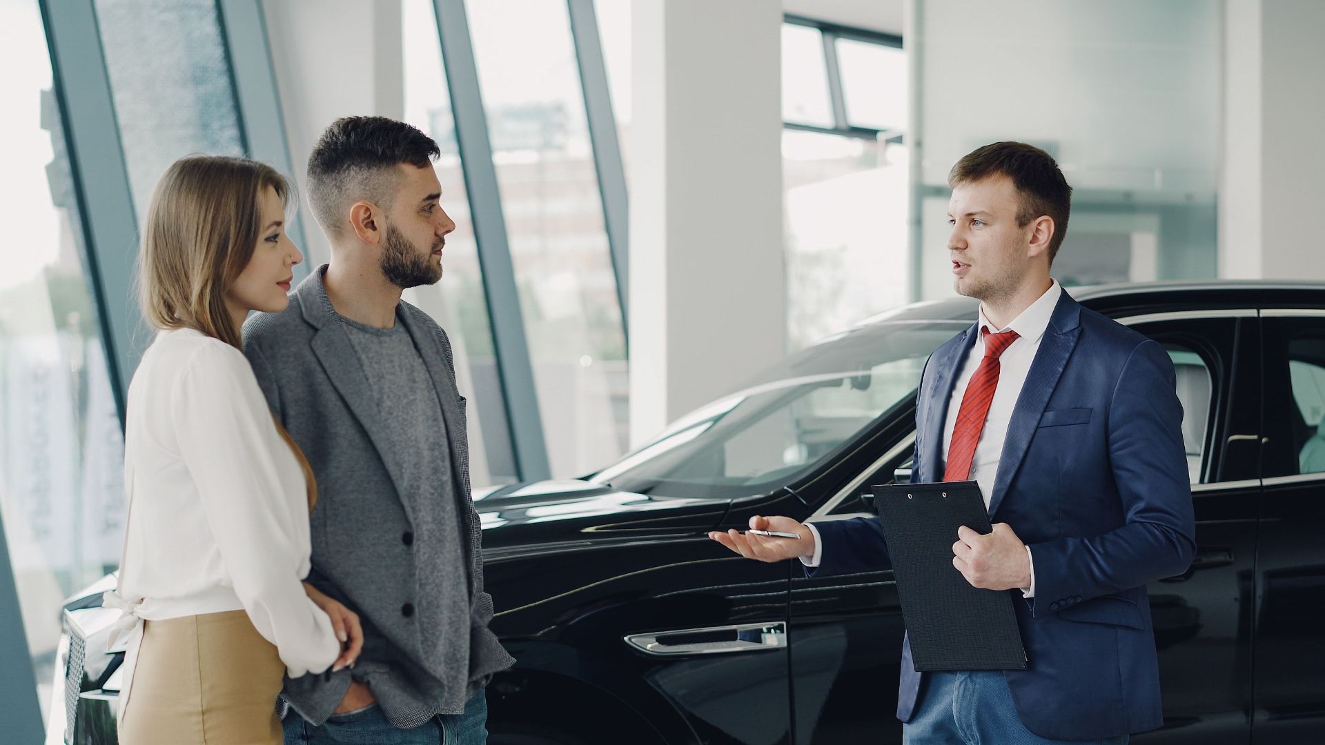 A couple talks with a salesman in a modern car showroom, considering a vehicle purchase.