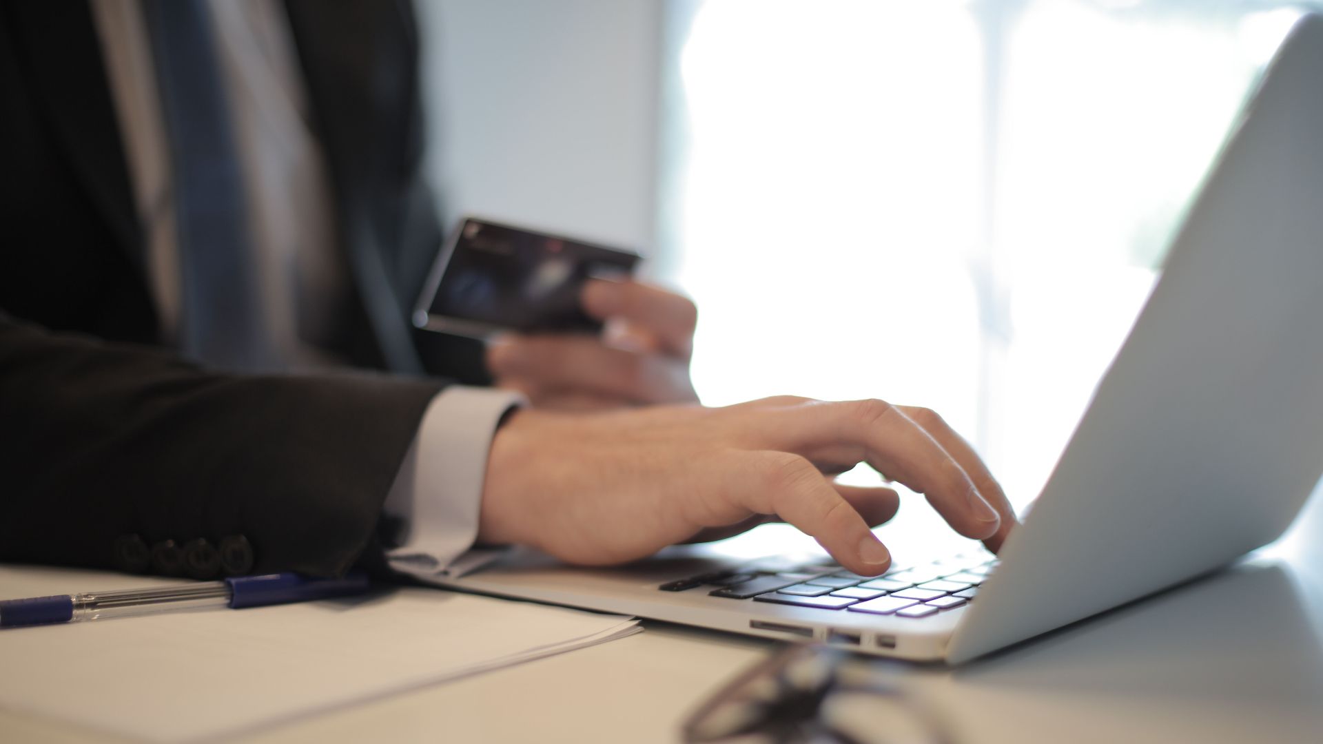 Man in suit using laptop and credit card for online transaction at work.