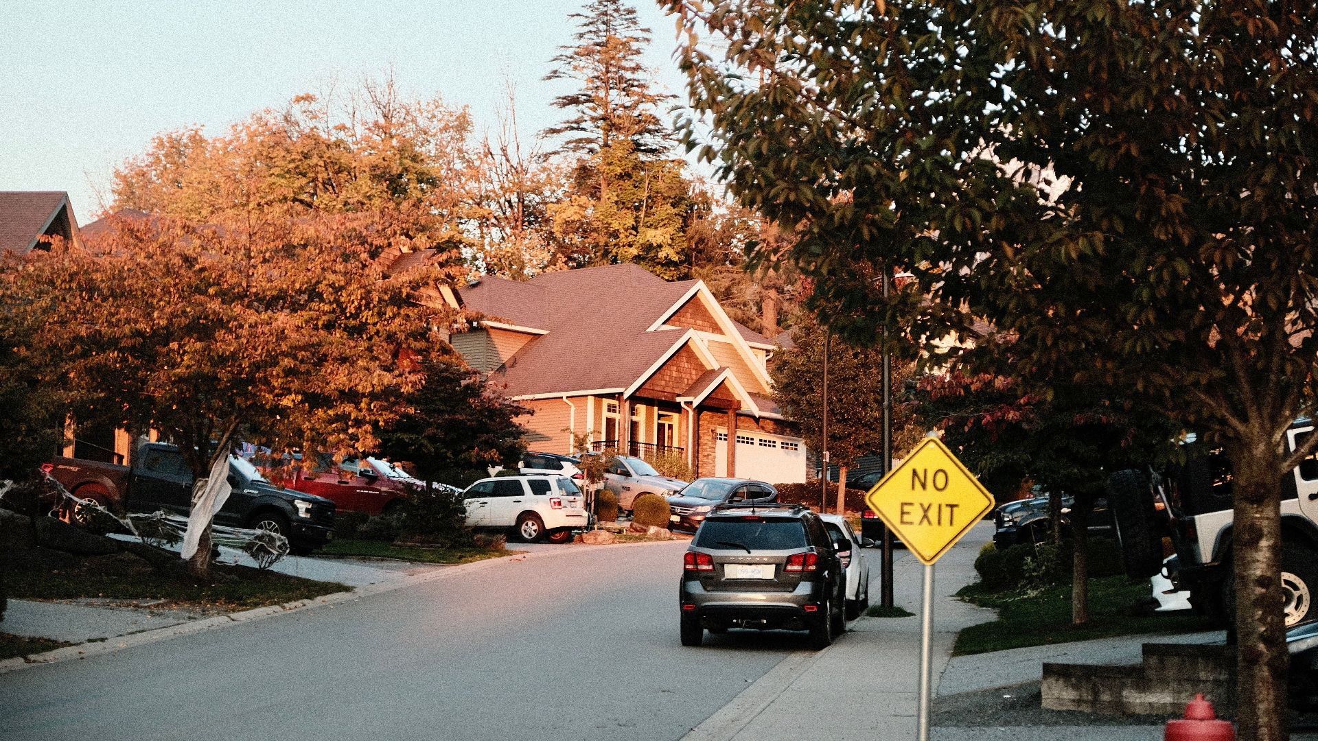 Charming suburban street scene with houses, cars, and a no exit sign in fall.