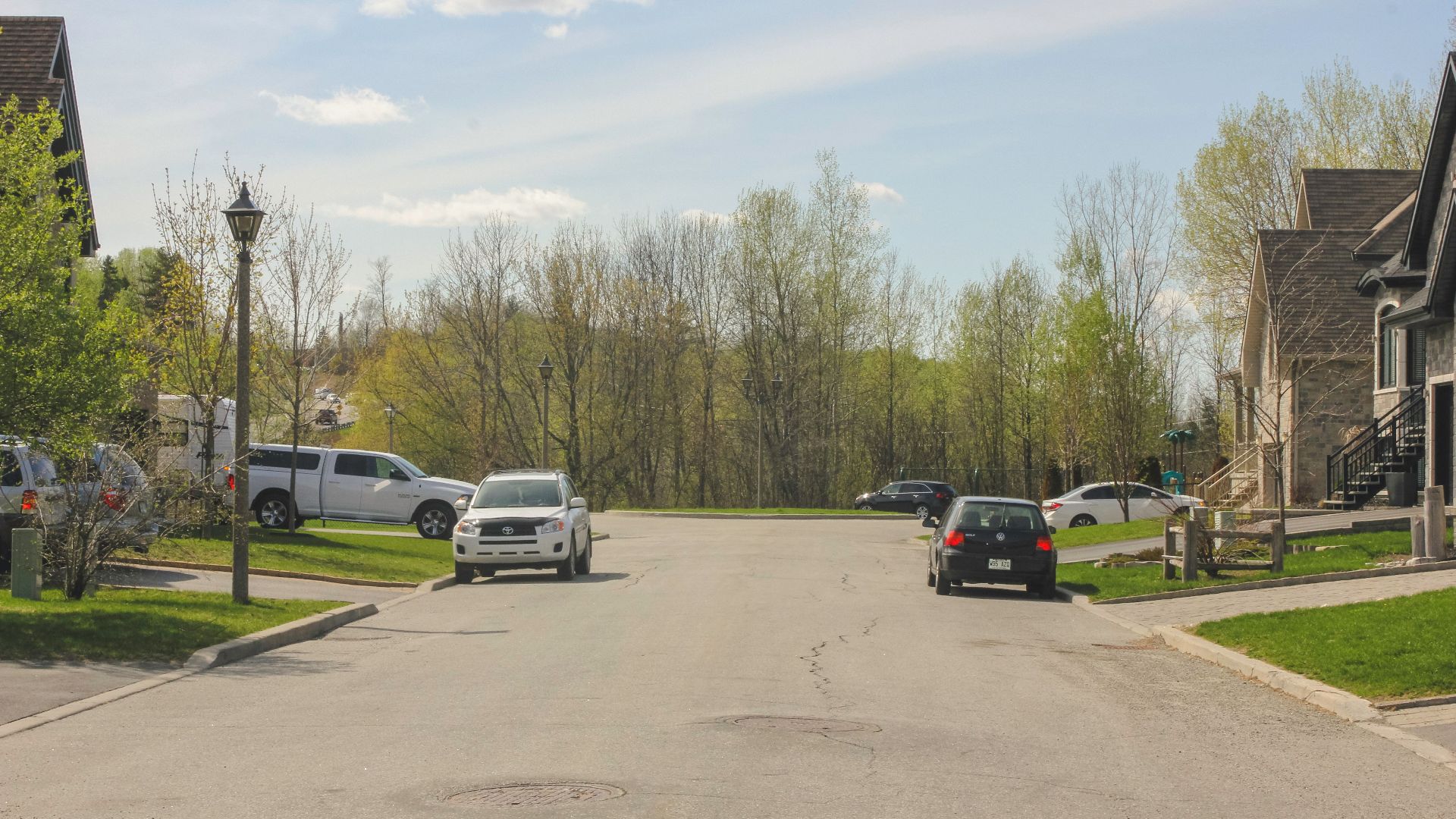 A peaceful suburban street in Gatineau, QC, Canada with parked cars and trees under a clear sky.