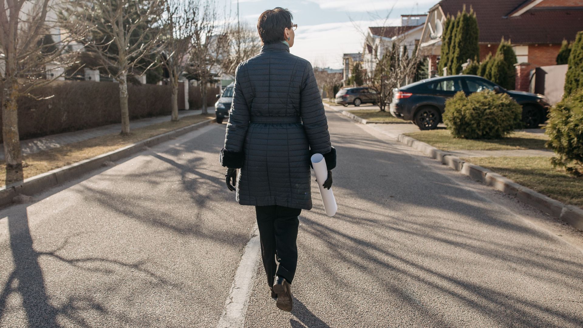 Back view of a woman walking down a suburban street on a sunny winter day.
