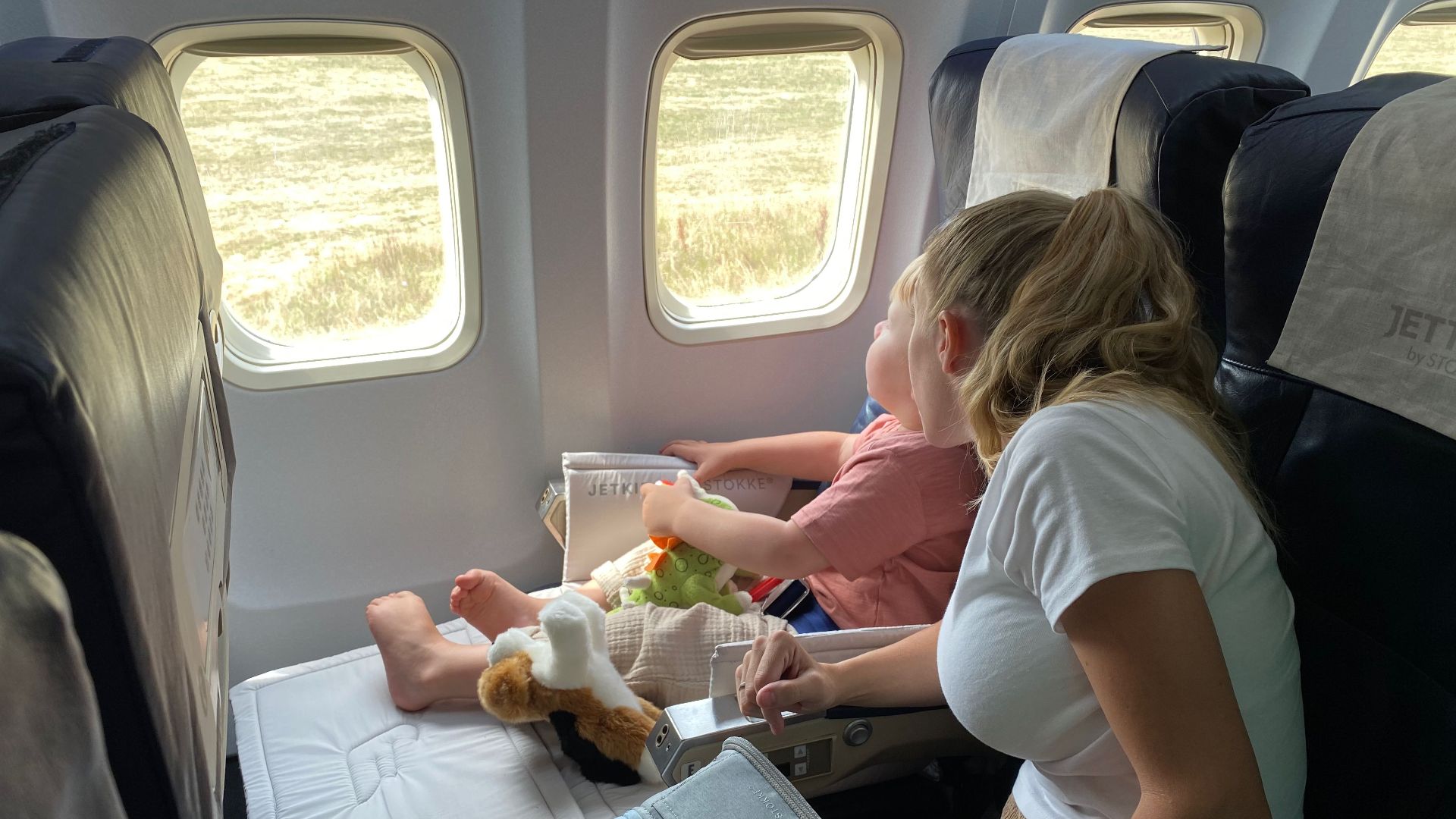 Mother and child sitting inside airplane, enjoying scenic view through windows during flight travel.