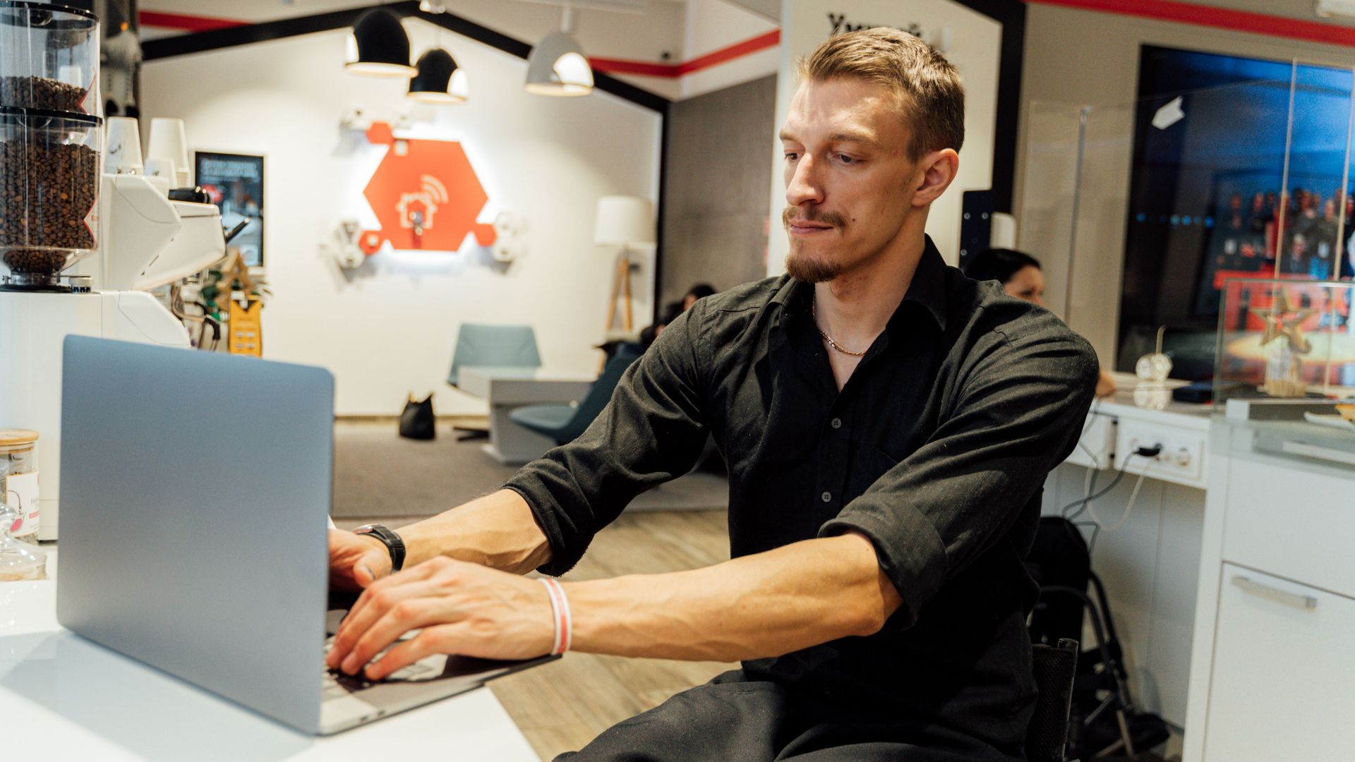 Man in a wheelchair using a laptop in a modern cafe, showcasing accessibility.