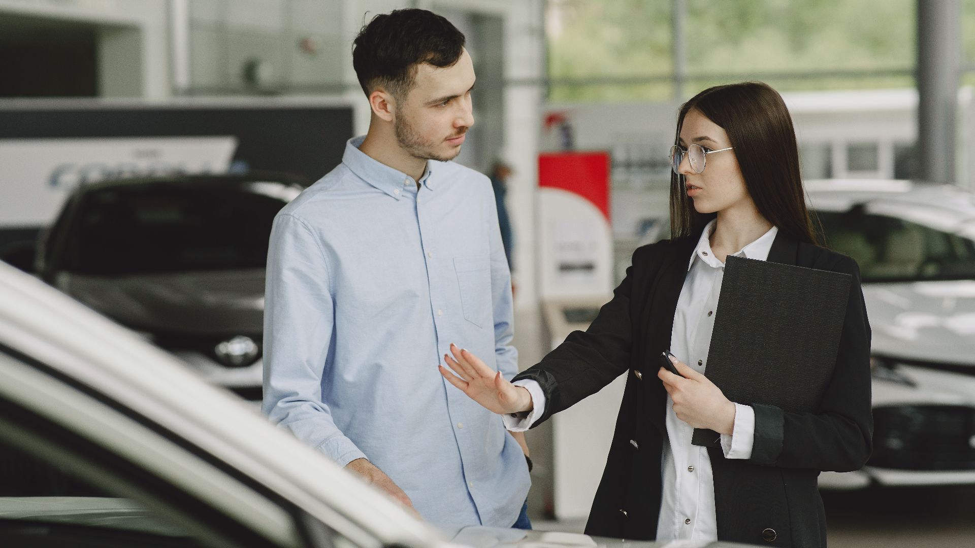 A salesperson and customer discussing car features in a dealership setting.
