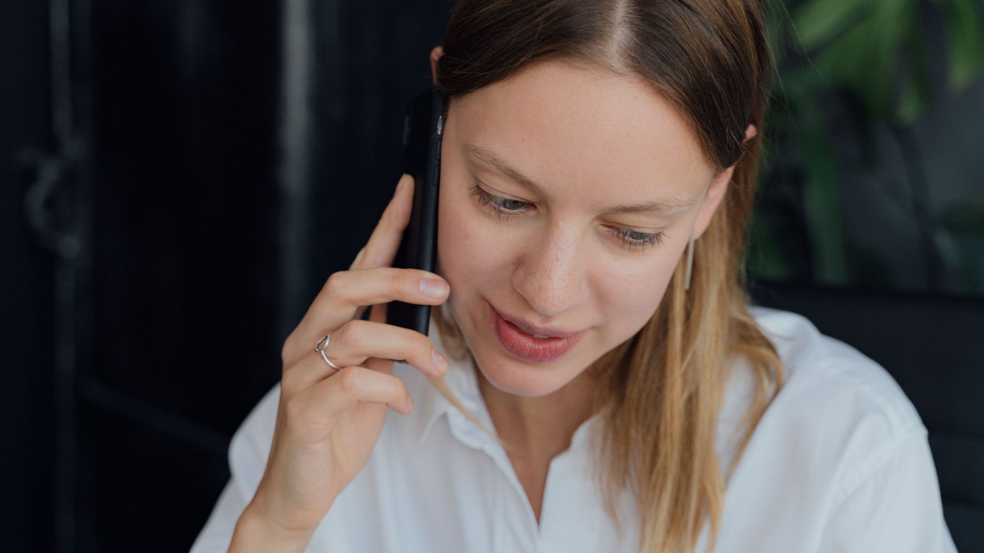A professional woman in a white shirt making a phone call in an indoor setting, showing communication and business engagement.