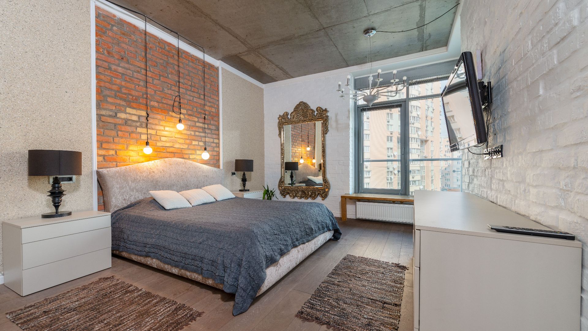 Spacious industrial-style bedroom with brick wall, cozy bed, and modern decor.