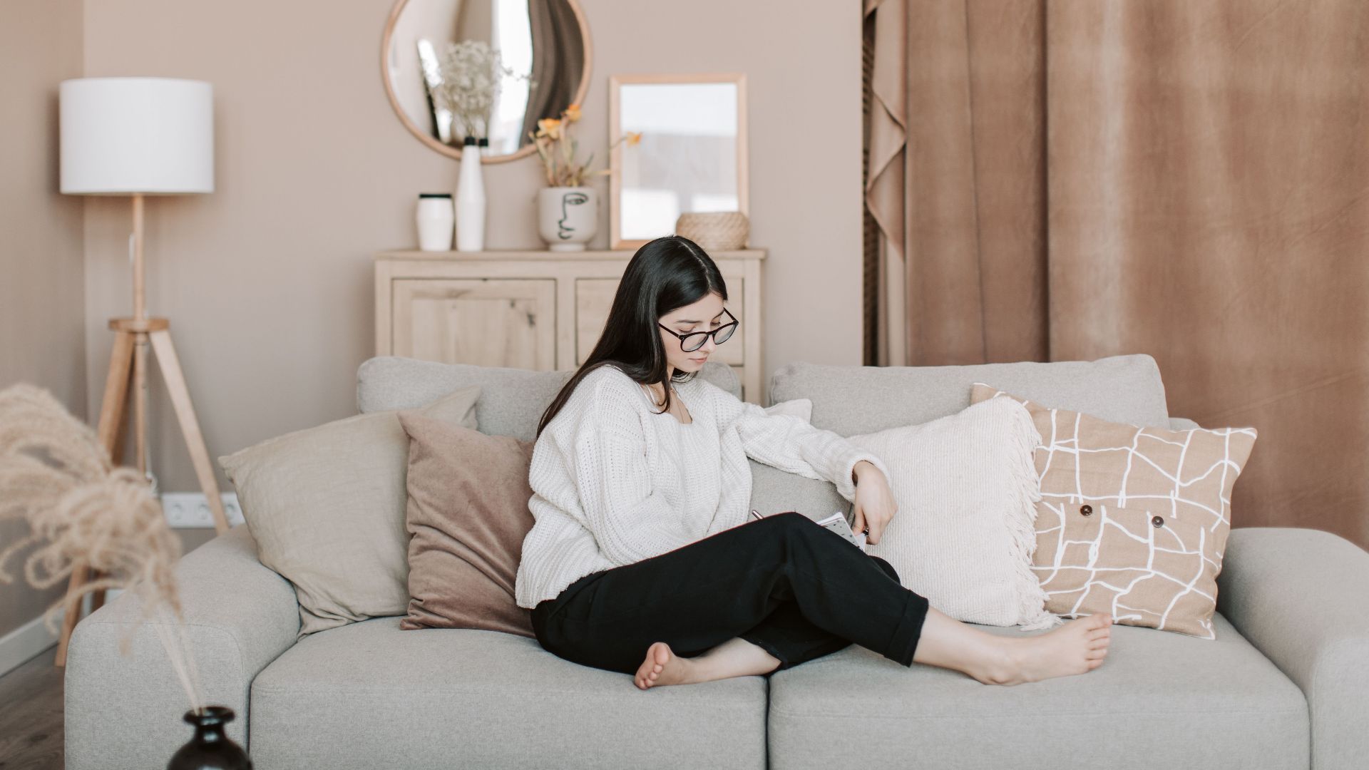 Young woman writing in notebook while sitting on a cozy sofa at home.