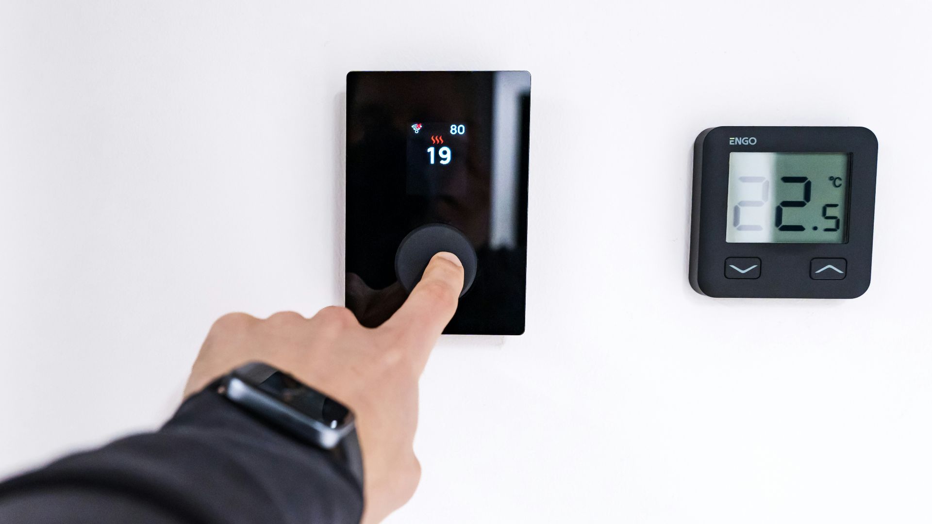 Finger adjusting a modern digital thermostat on wall