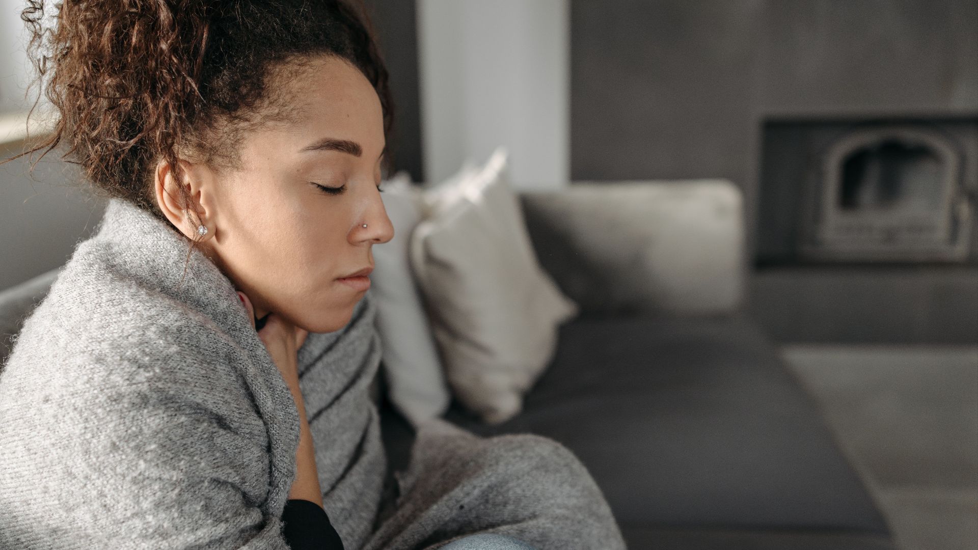 Young woman resting at home, wrapped in a blanket and feeling unwell, conveying a sense of illness or discomfort.