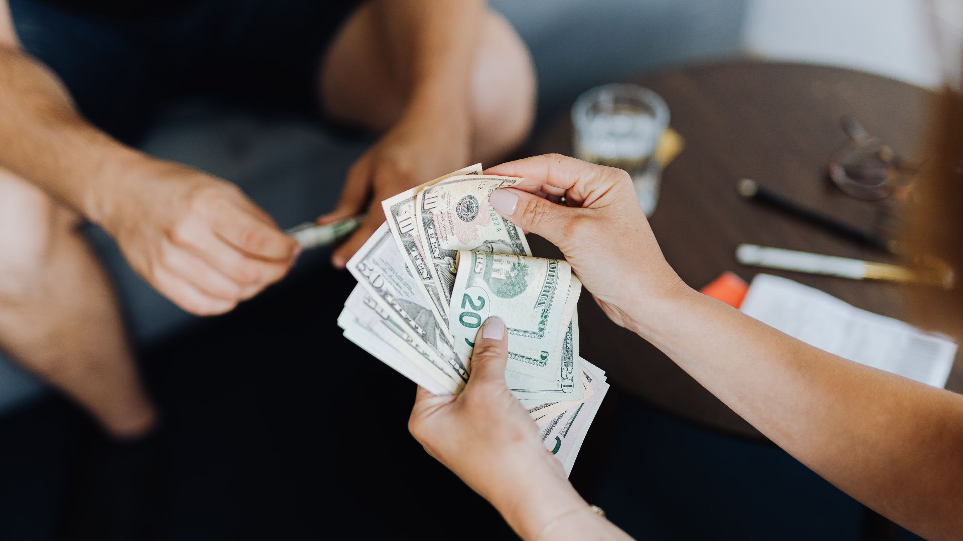 Close-up of people handling and counting US dollar bills indoors.