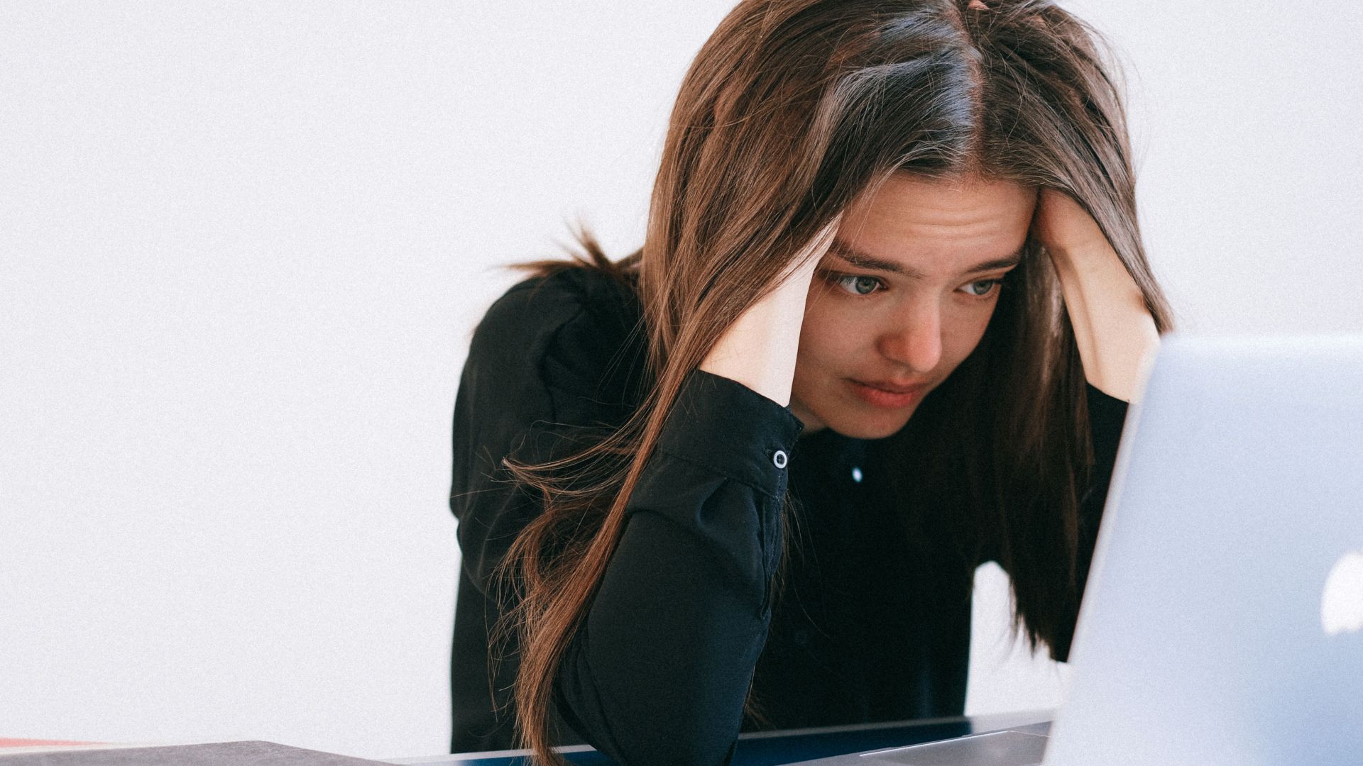 A stressed woman at a desk, looking at a laptop with a worried expression.